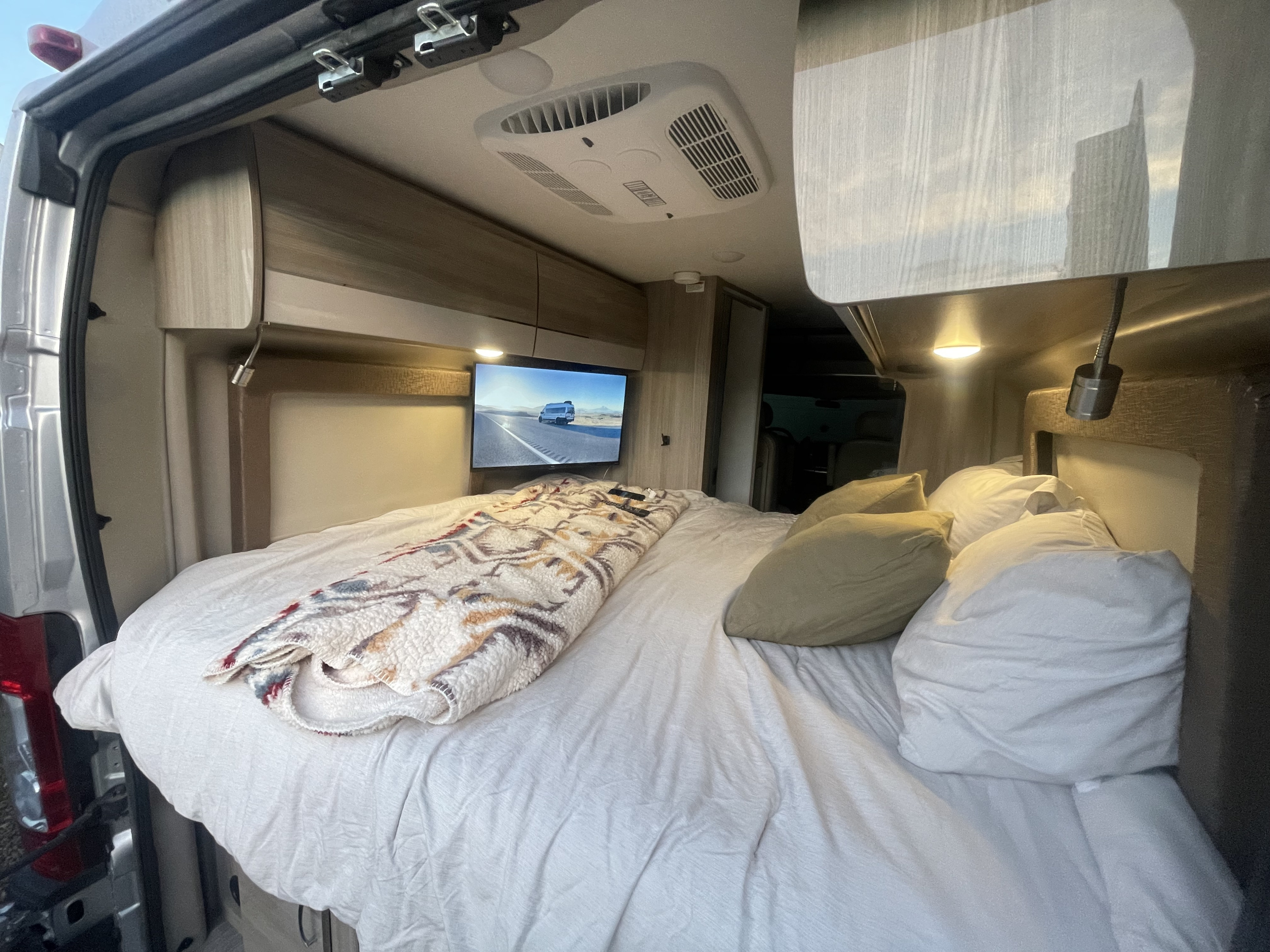 Relax in this comfy RV rental! Interior view of a van's bed, TV, and overhead AC unit with open rear doors.. Thor Sequence 2021