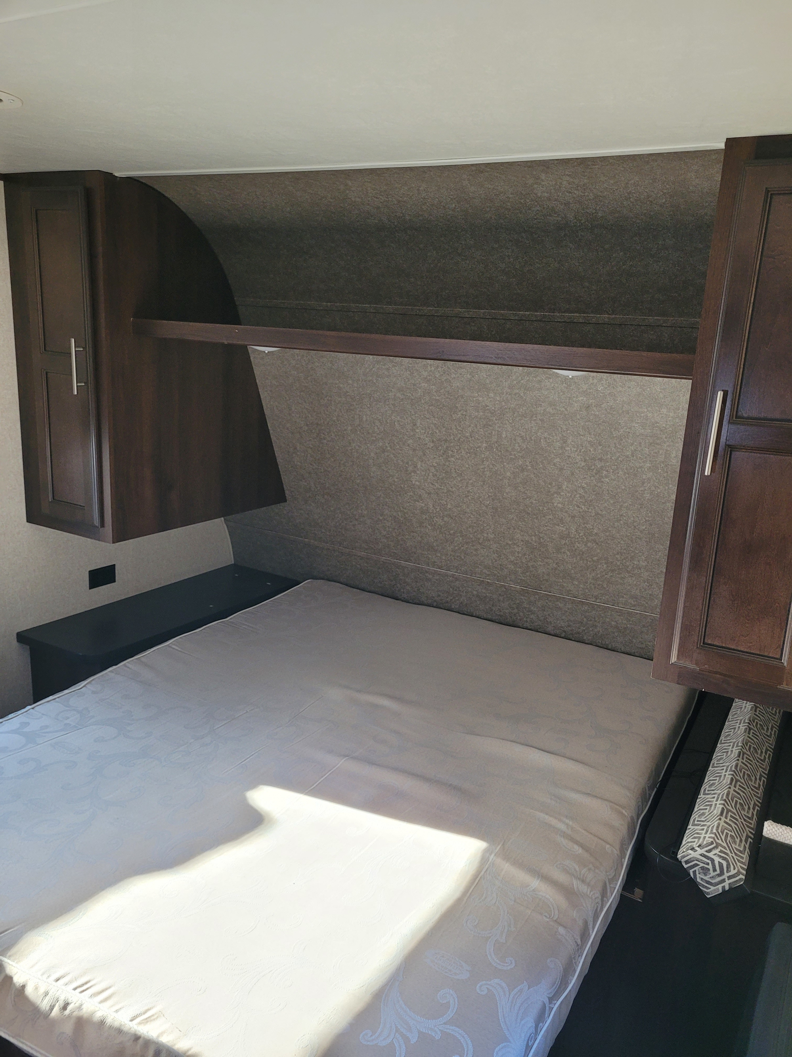 RV rental bedroom interior: a compact bed, dark overhead cabinets, and a bedside shelf.. Jayco Jay Flight SLX 2018