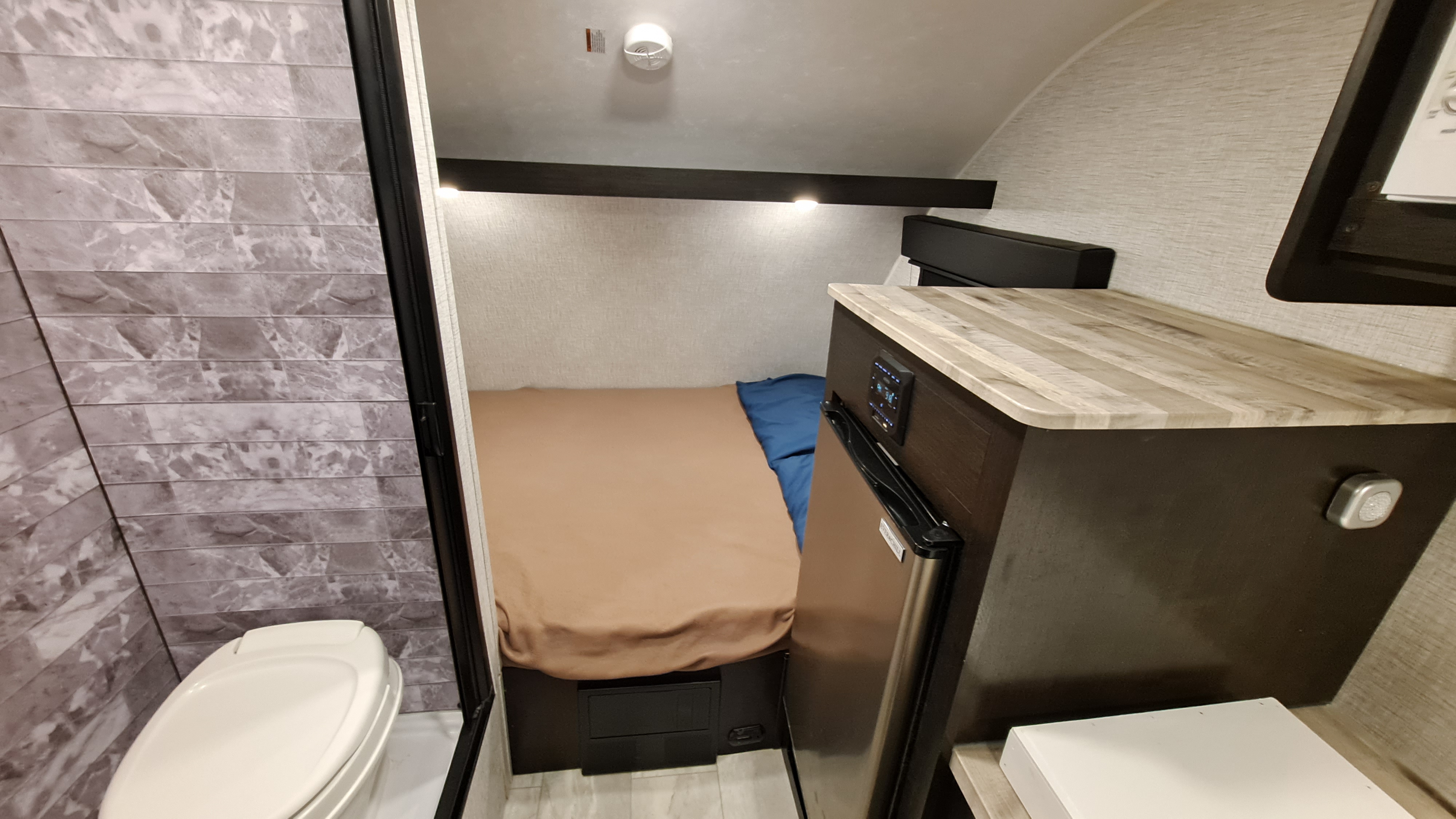 Inside a cozy RV rental: features a bed, kitchenette with fridge, and compact bathroom with toilet.. Braxton Creek Free Solo Plus 2022