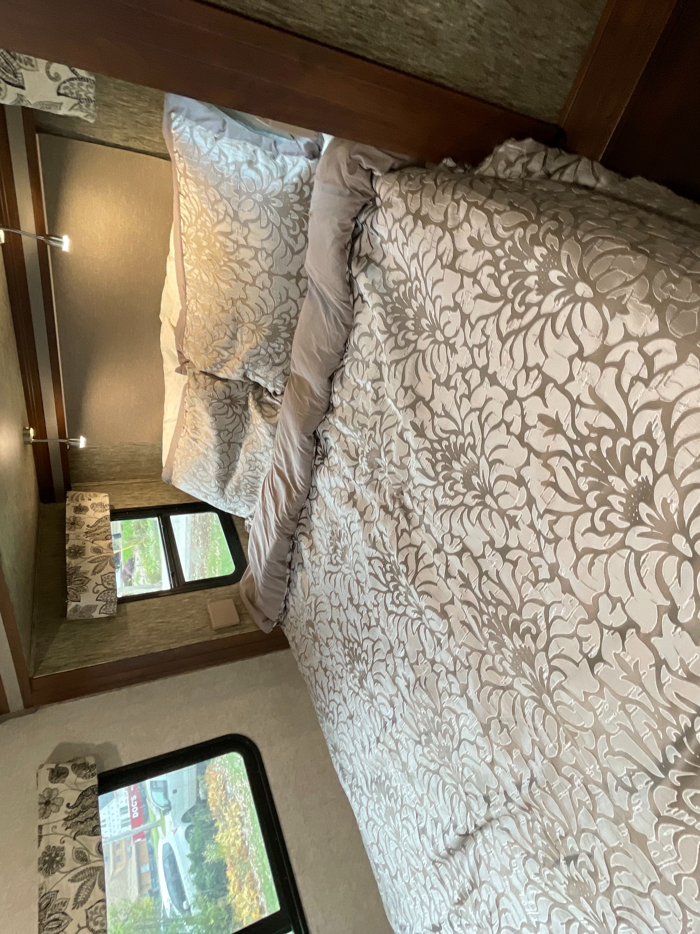 Cozy RV rental bedroom with patterned bedding, illuminated by wall sconces, offering views of the outdoors.. Forest River Sunseeker TS 2020