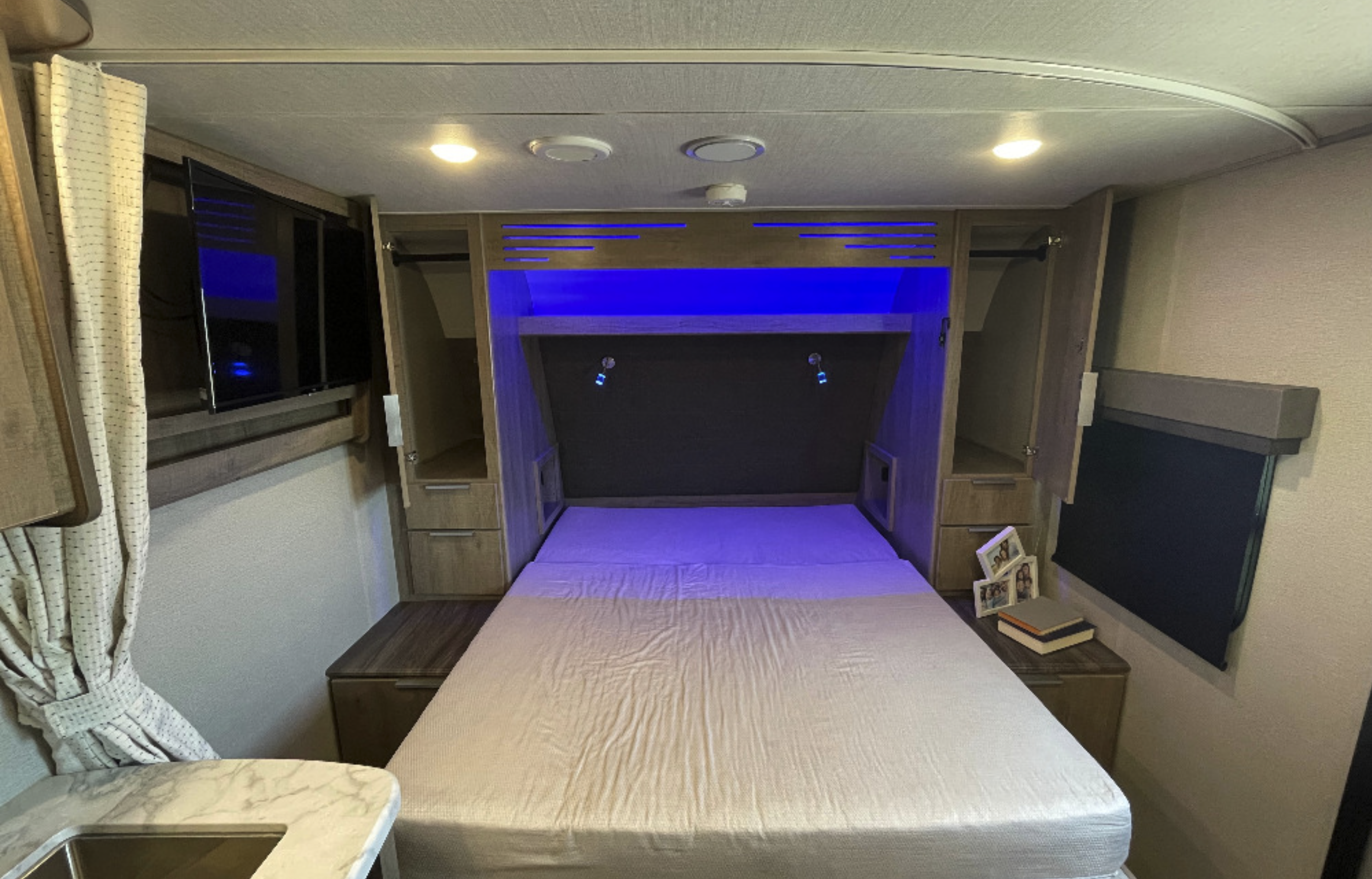 RV rental bedroom interior: a comfortable bed with blue accent lighting, built-in storage, and wall-mounted TV.. Grand Design Imagine XLS 21BHE 2022