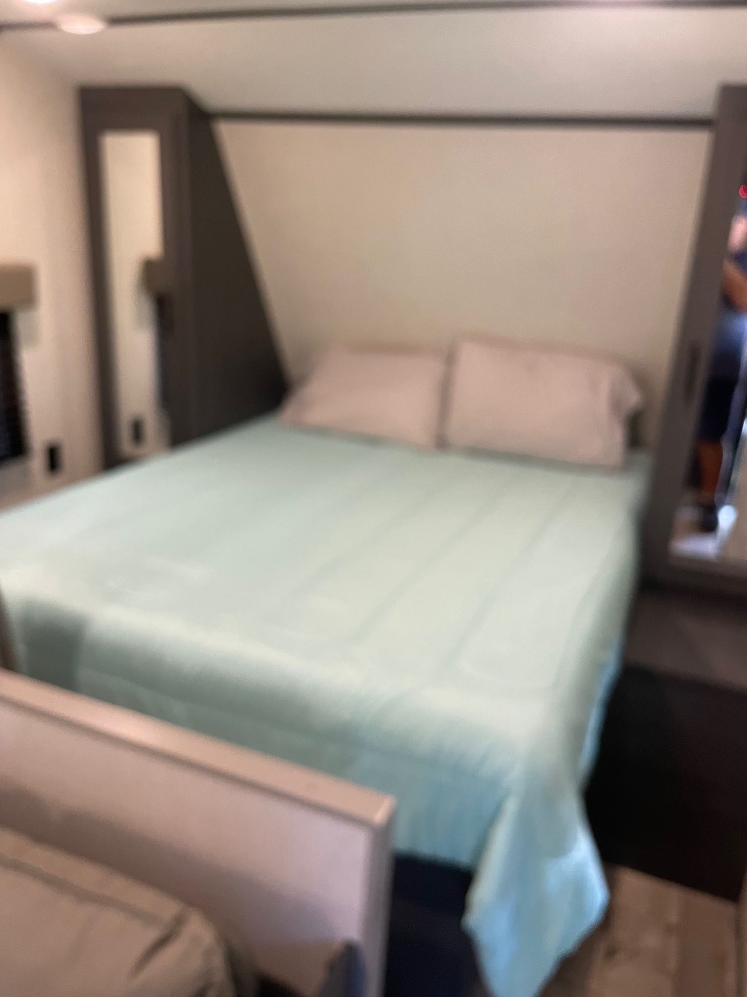 Inside an RV rental, a neatly made bedroom features a bed with light blue bedding, flanked by dark storage units.. Dutchmen Aspen Trail 25 BH 2022