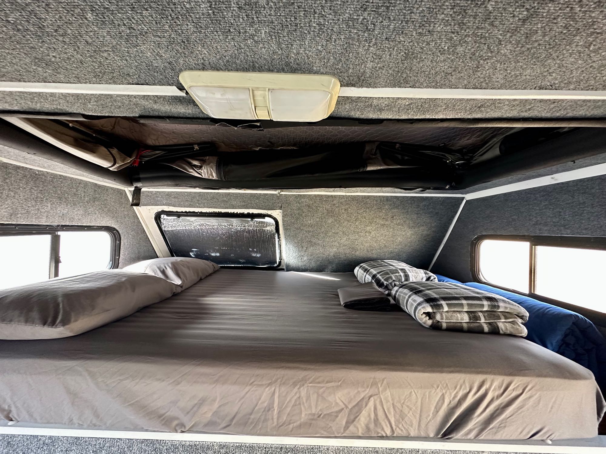 Inside this rv rental: A neatly made bed with gray linens, pillows, blankets, and practical overhead storage.. Four Winds Majestic 2004