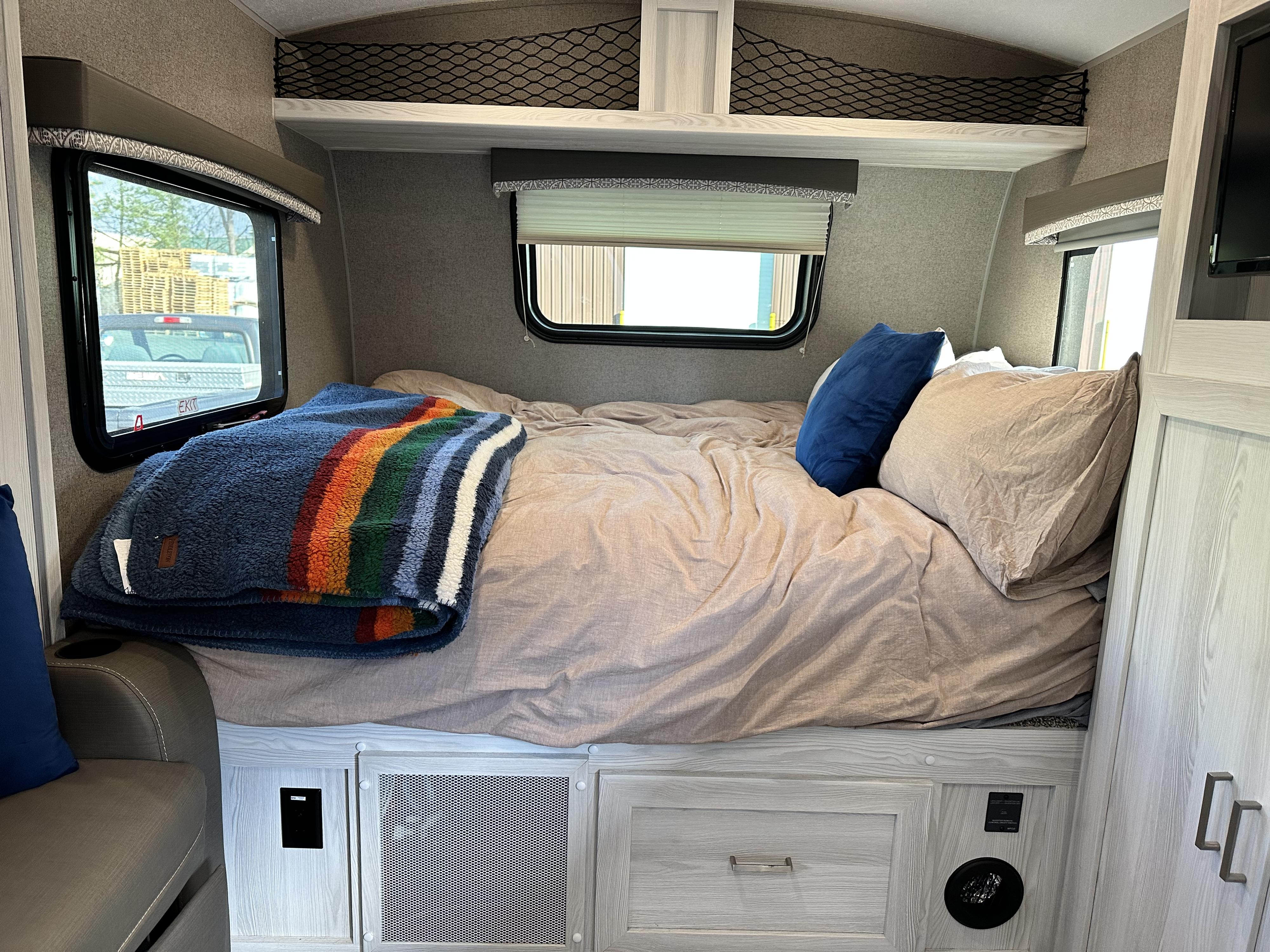 Inside an RV rental bedroom, featuring a comfortable bed with a colorful blanket, windows, and ample storage.. Forest River Rockwood Geo Pro 2020
