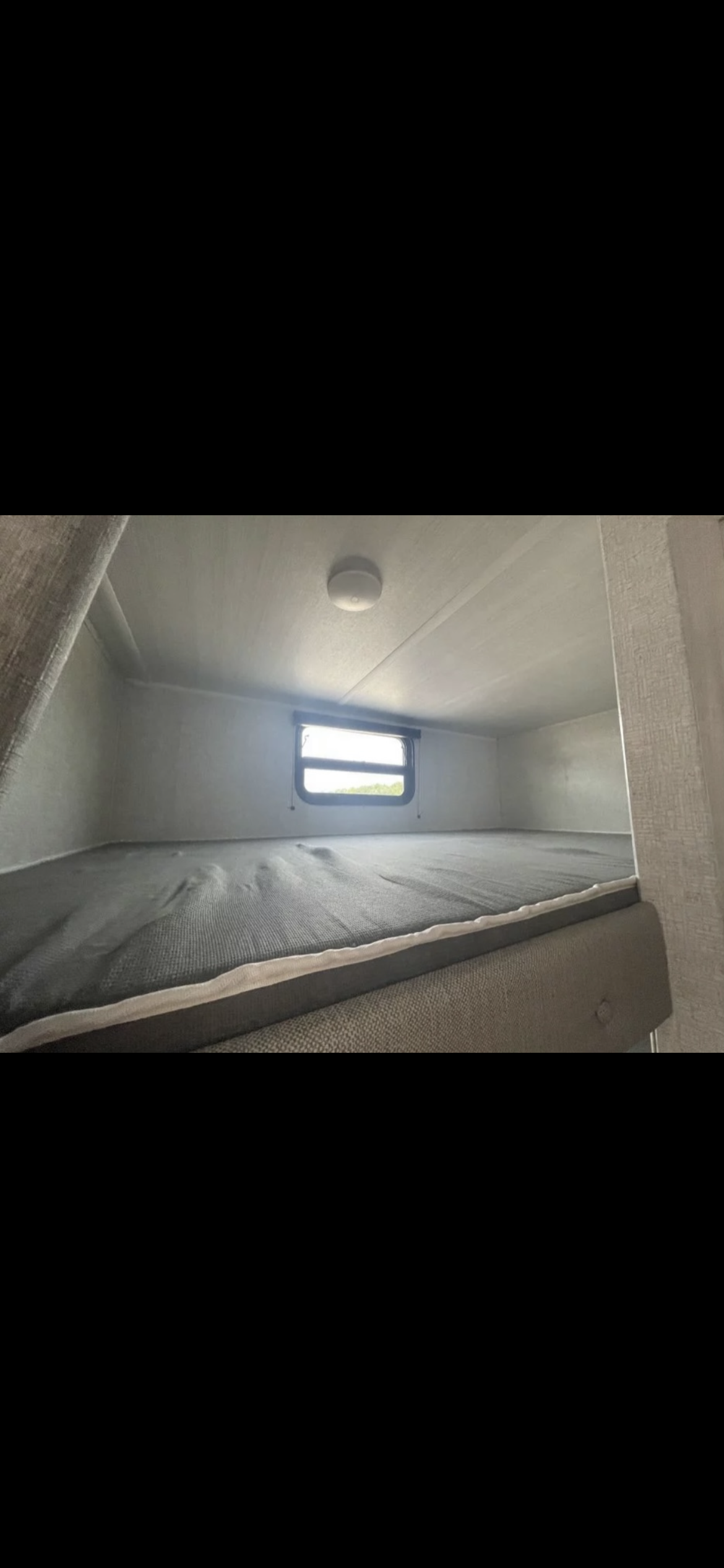 RV rental bunk bed interior: gray mattress, window with outdoor view, and ceiling light. Perfect for camper adventures.. Forest River Della Terra 2022