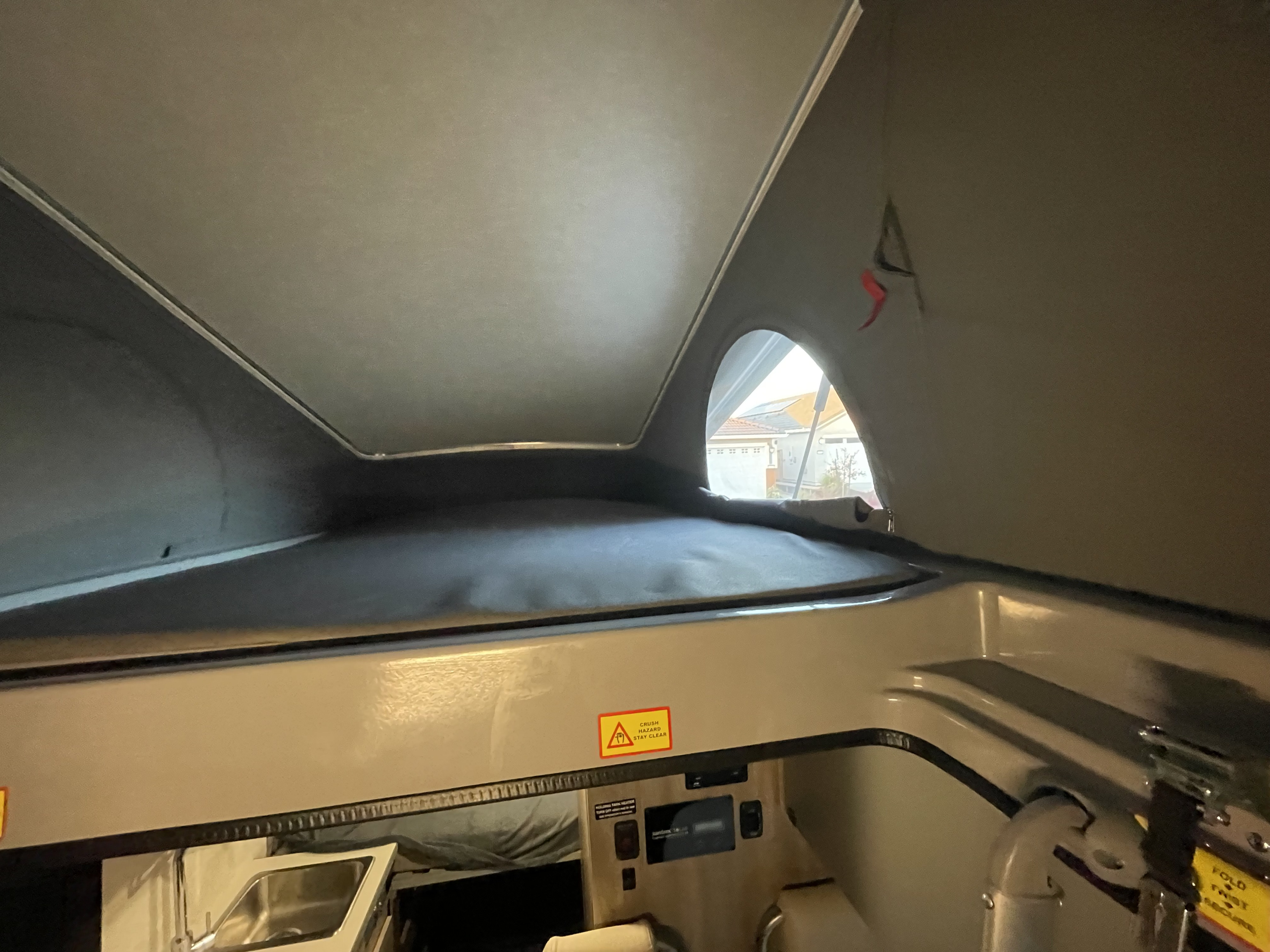 Inside a pop-top RV rental, featuring an elevated sleeping area with a mattress, a view out the window, and lower controls/sink.. Winnebago Winnebago 2023