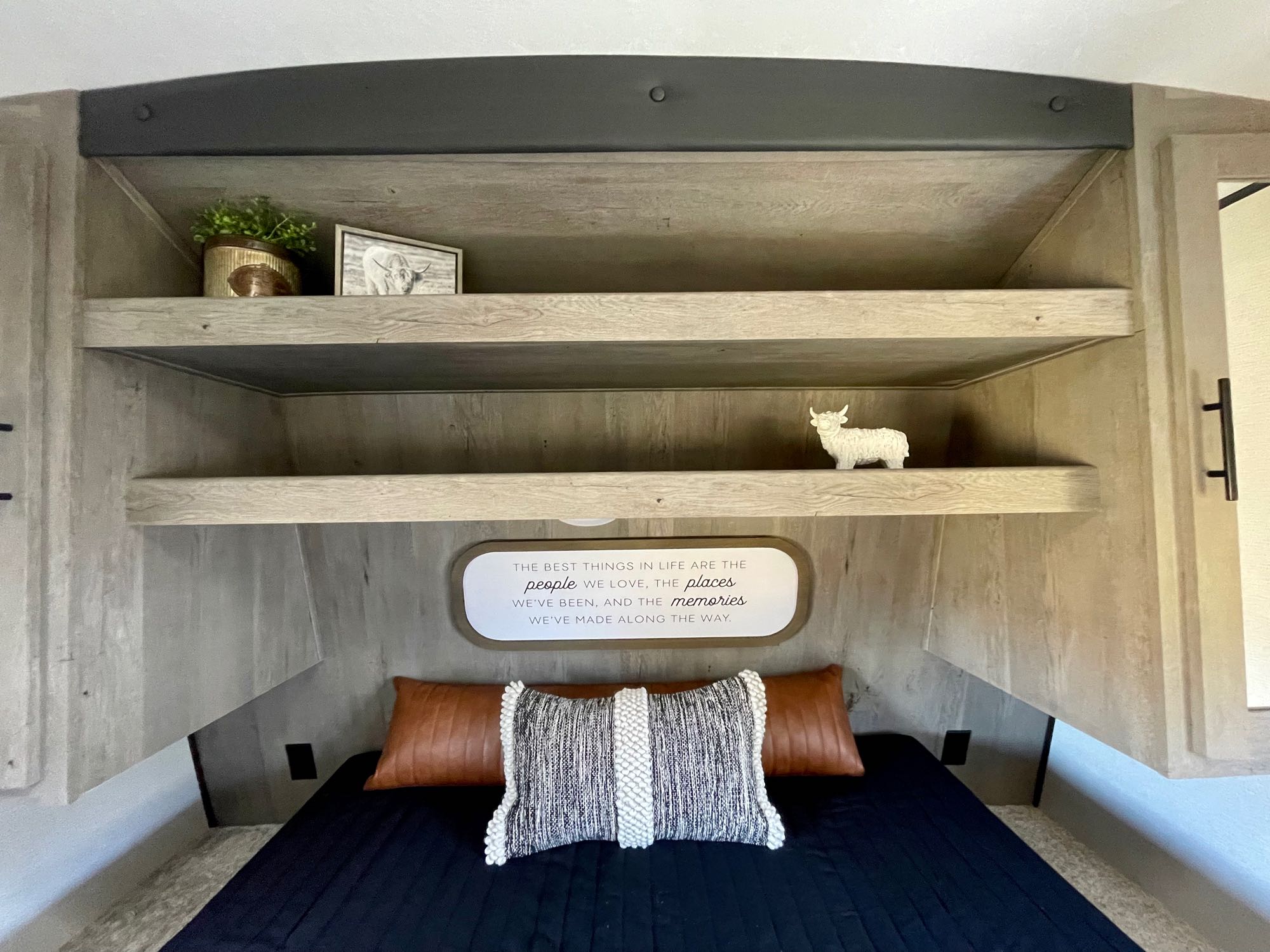 Cozy RV rental bedroom with built-in shelves, decorative accents, and a heartwarming quote about memories above the bed.. Keystone RV Springdale 2021