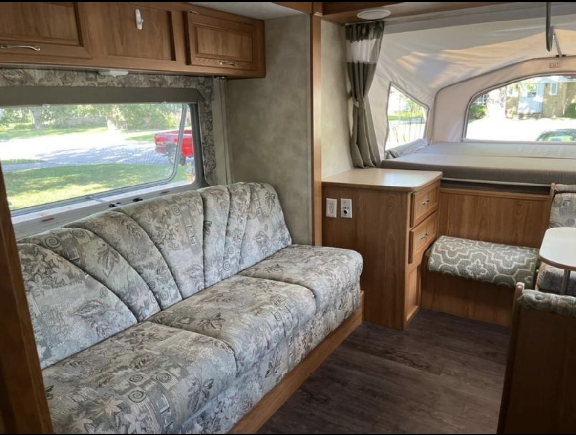 Cozy RV rental interior: features a patterned sofa, wood cabinets, and a comfortable pop-up bed area with large windows.. Forest River Palomino Stampede 2005