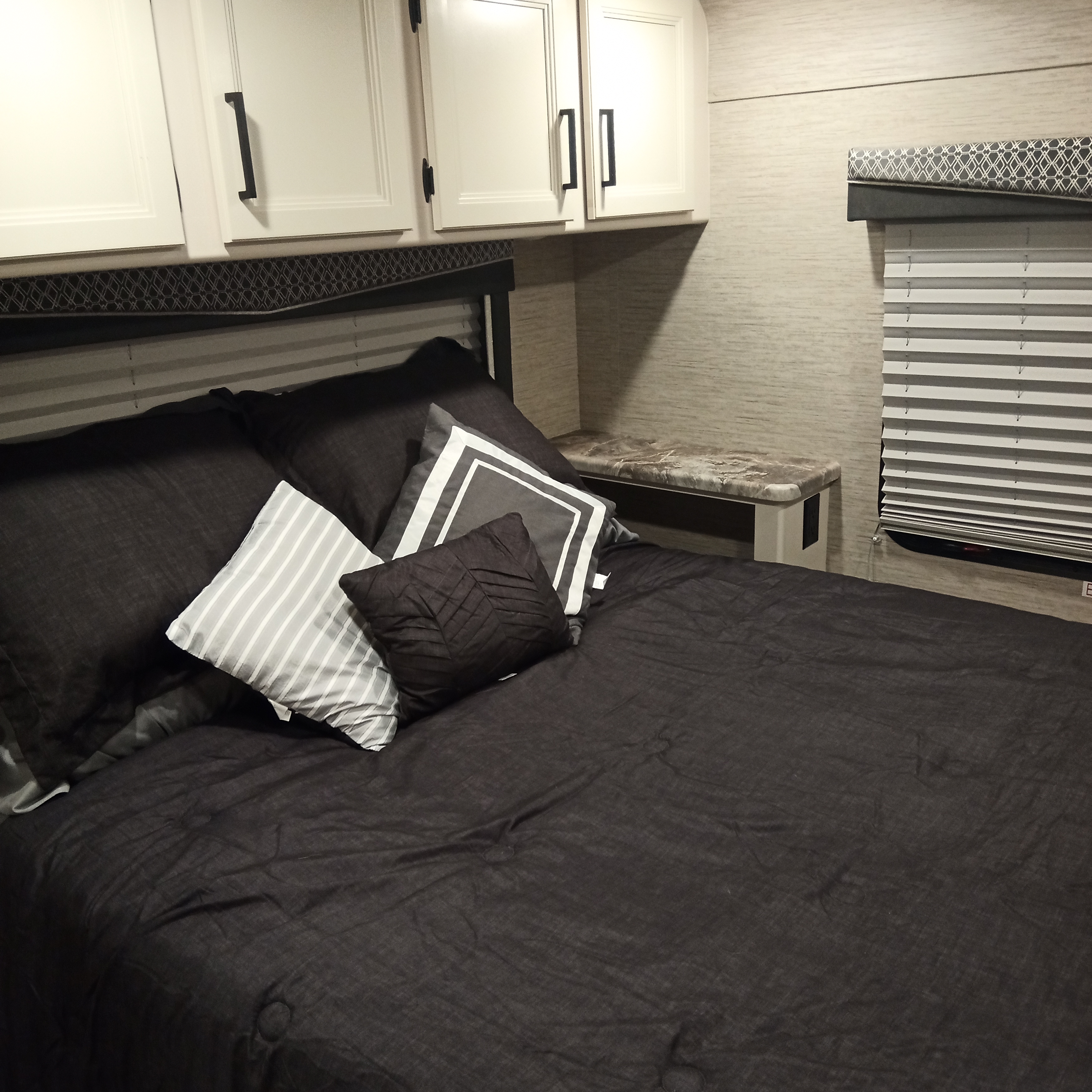Modern RV rental bedroom with dark bedding, sleek white cabinets, and a side table. Offers a cozy space for travel.. Thor Four Winds 2022