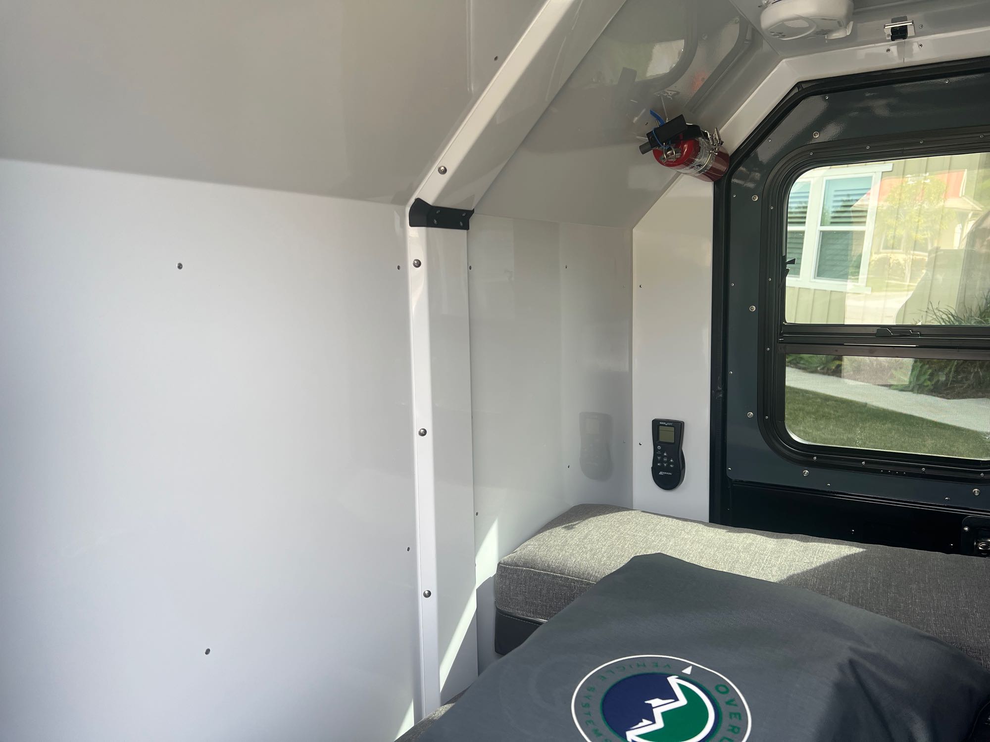 Inside a compact RV rental, showing the bed, window with exterior view, and control panel for comfortable travels.. Off0Grid Explorer 2.0 2022