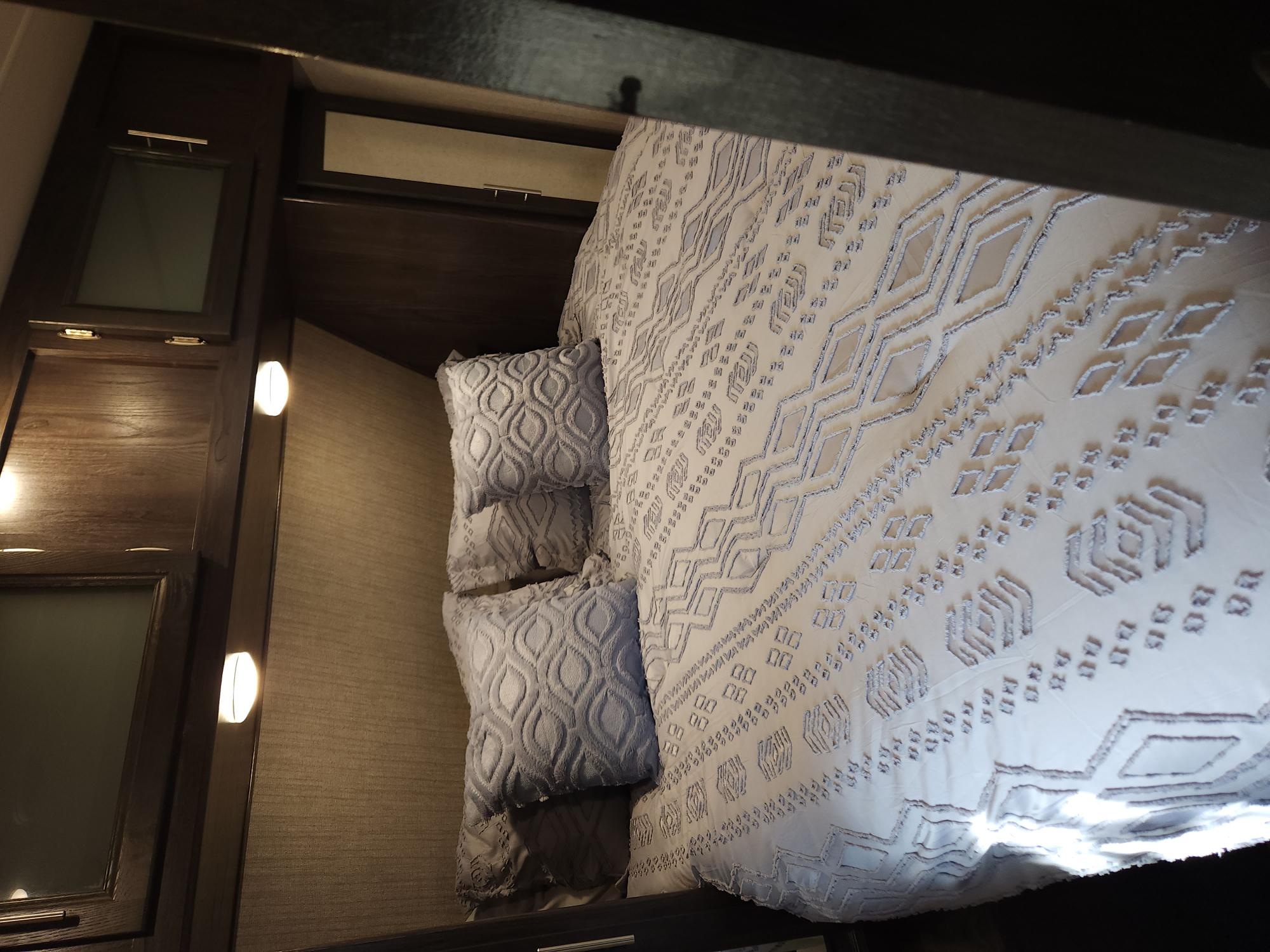 Cozy RV rental bedroom with a white patterned comforter, soft pillows, and illuminated wooden storage cabinets.. Dutchmen Kodiak Ultra Lite 2019