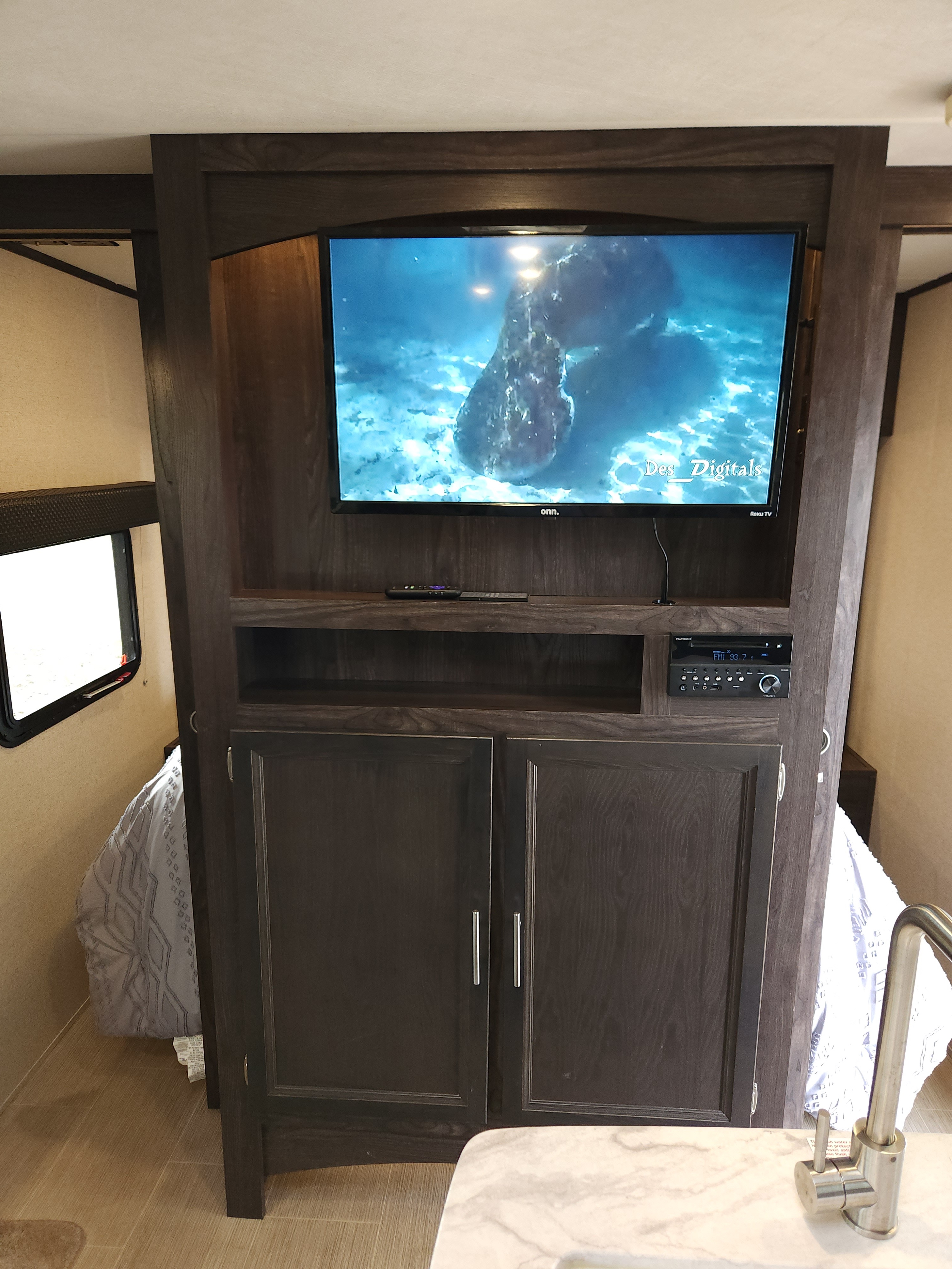 RV rental interior: A dark wood entertainment center with TV, stereo, and storage, flanked by compact sleeping areas.. Dutchmen Kodiak Ultra Lite 2019