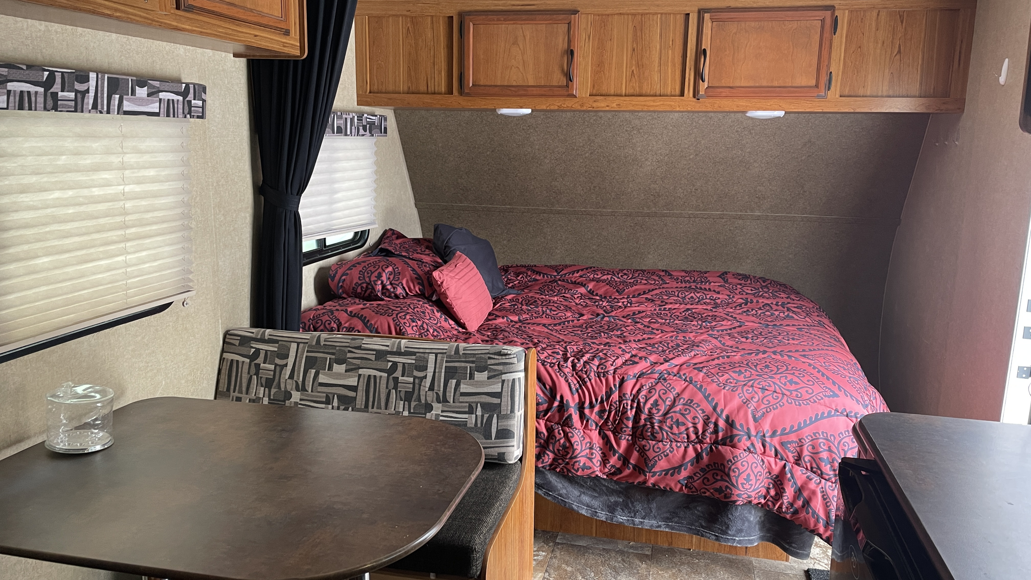 Cozy RV rental interior: main bed with red bedding, overhead cabinets, and dining area with patterned seating & table.. Starcraft AR-One Maxx 2016