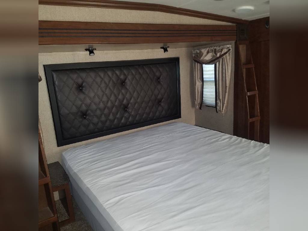 RV rental bedroom featuring a large bed with a dark, quilted headboard, window, and wooden ladder for access.. Heartland RVs Gateway 2015