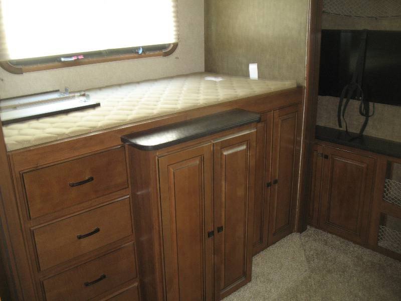 Cozy RV rental bedroom features a raised bed, built-in storage drawers & cabinets, plus a mounted TV area.. Heartland RVs Gateway 2015