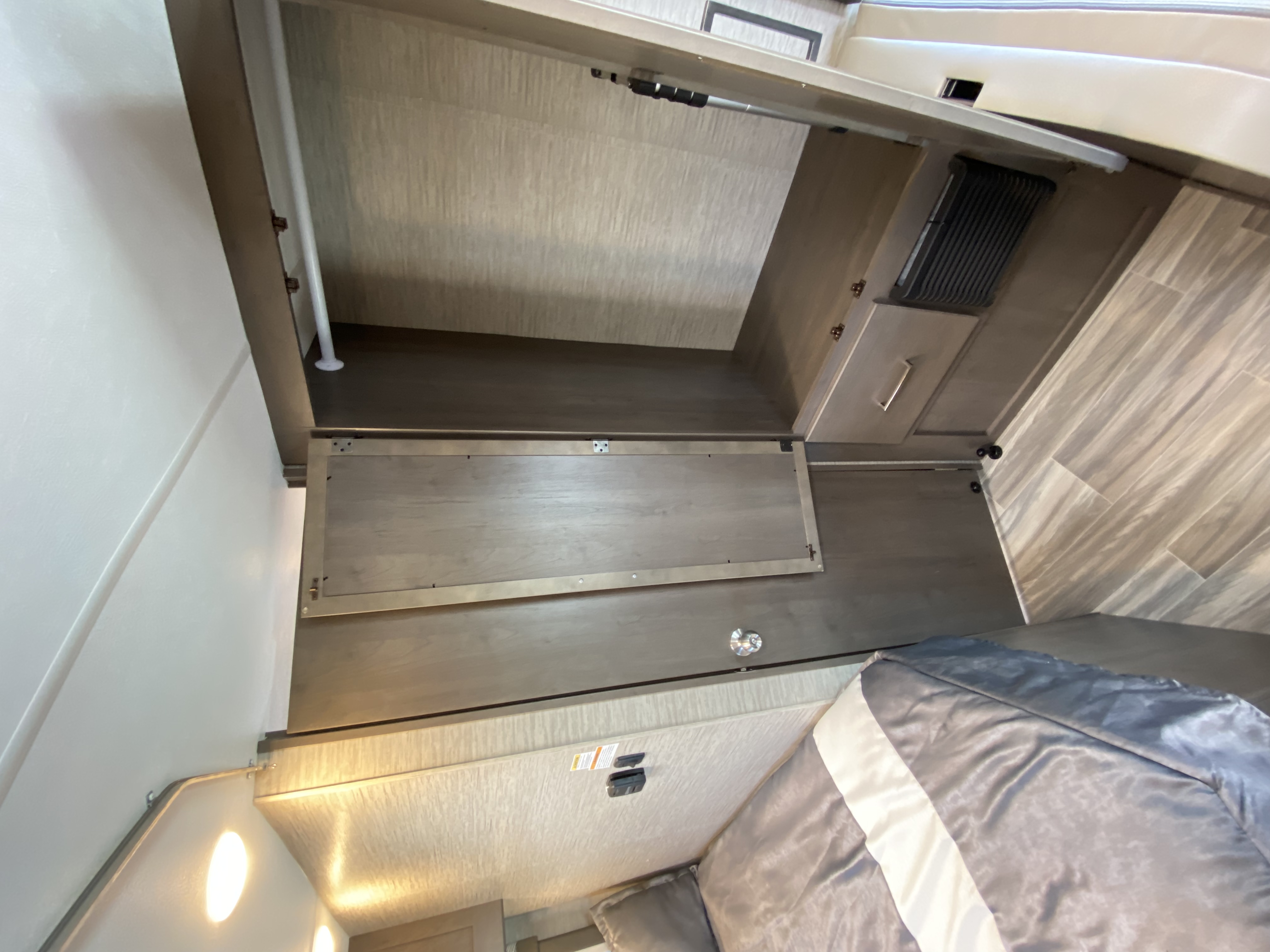 Modern RV rental bedroom interior with a lift-up bed base for storage, light-toned cabinets, and wood-look flooring.. Thor Motor Coach Four Winds 2024