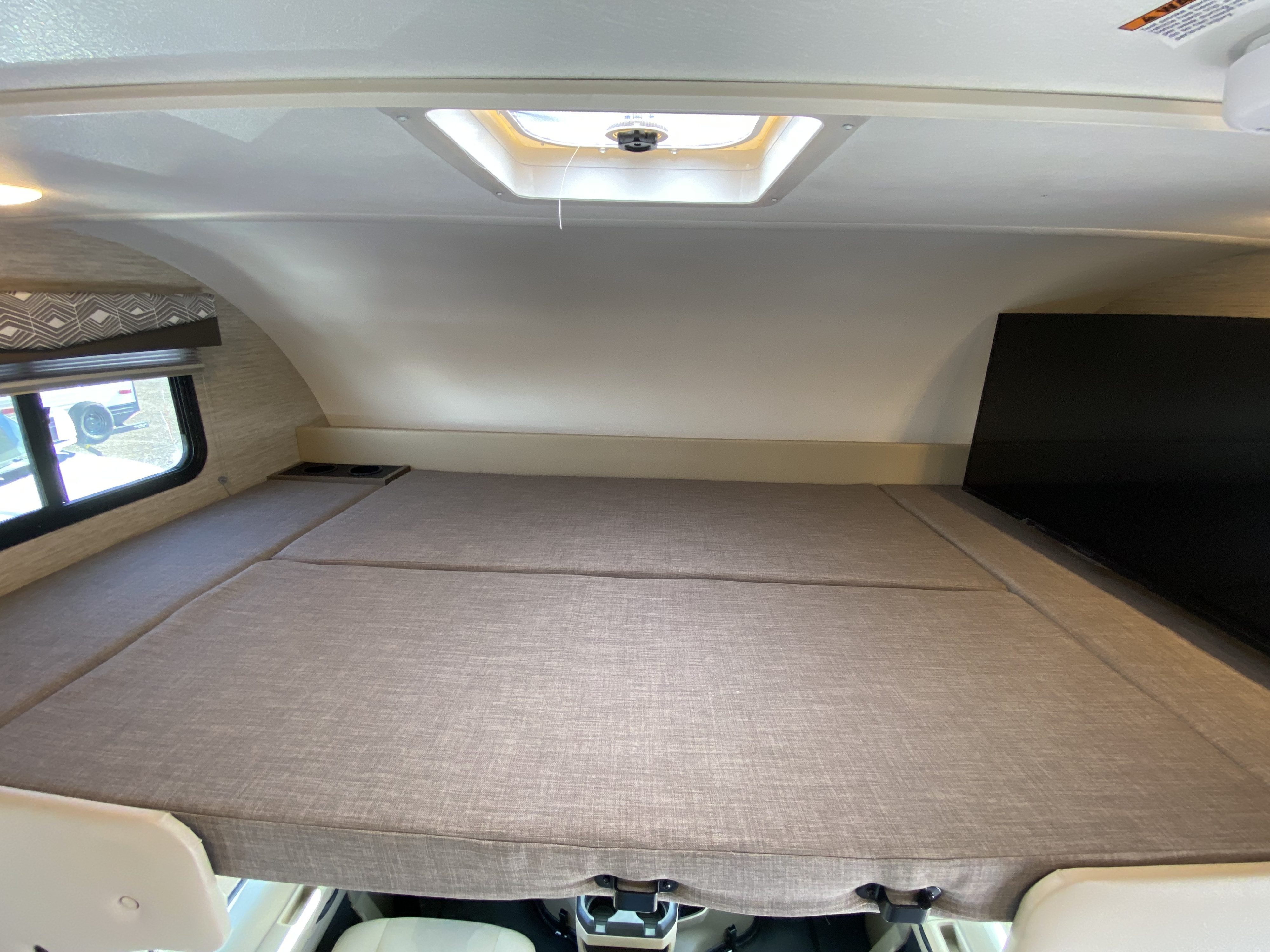 Overhead bunk sleeping area in an RV rental, featuring a comfortable bed, window, and roof vent.. Thor Motor Coach Four Winds 2024