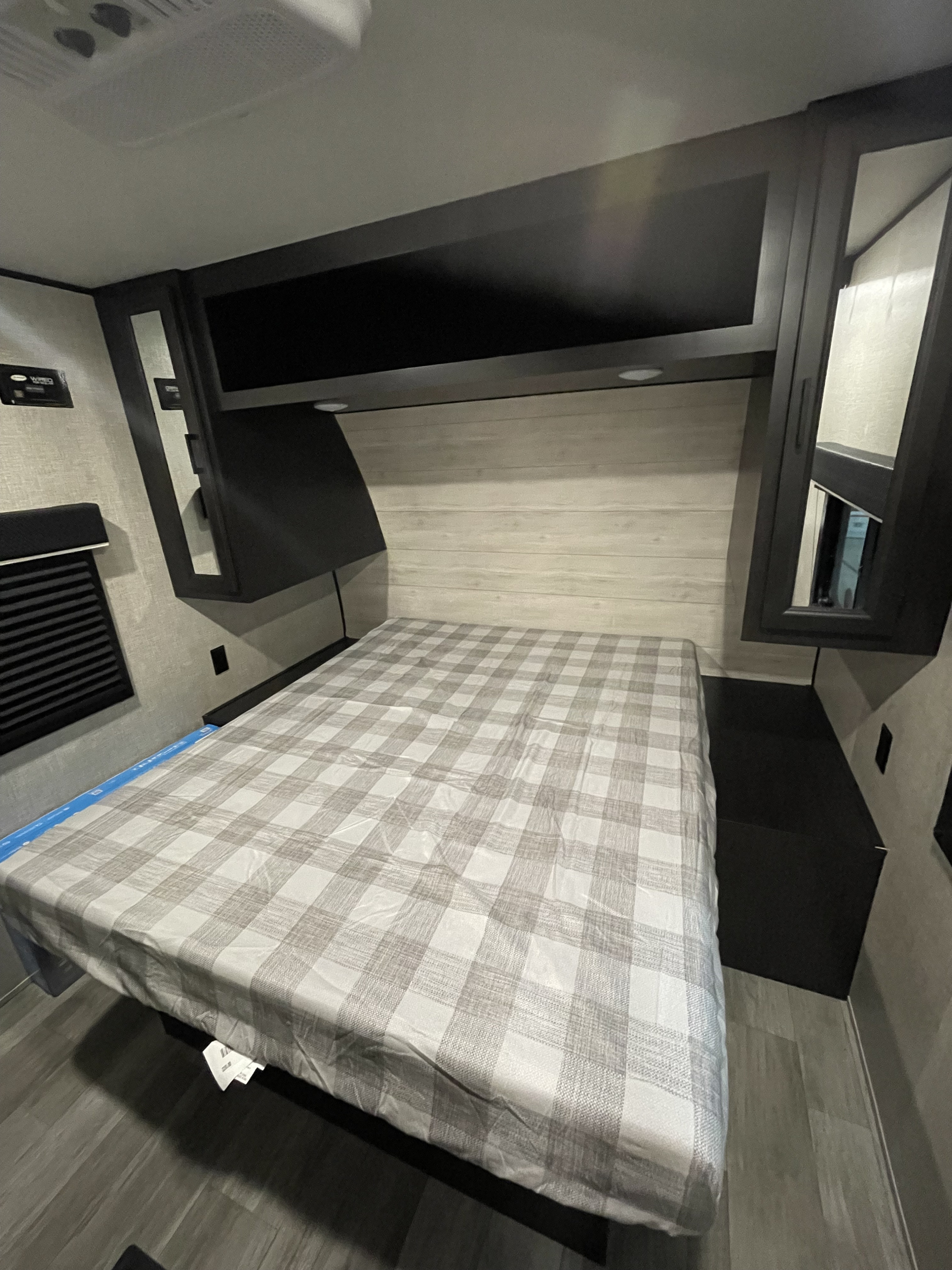 Inside an RV rental: a modern bedroom with a comfortable plaid bed, ample overhead storage, and mirrored cabinets.. Jayco 324DBS 2023