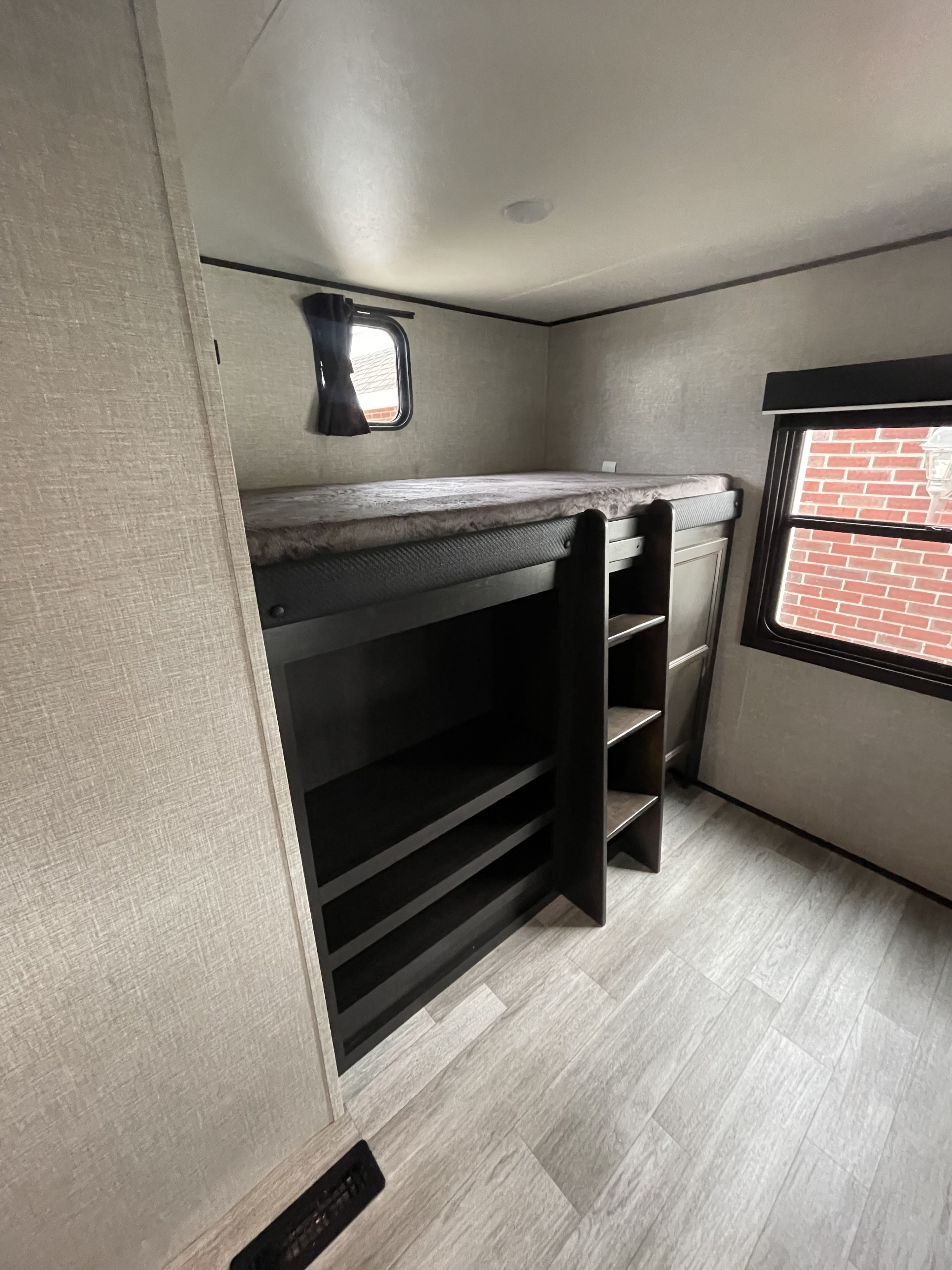 RV rental's bunk bed with integrated shelving, ladder, and windows, in a modern light-toned bedroom, ideal for family trips.. Jayco 324DBS 2023