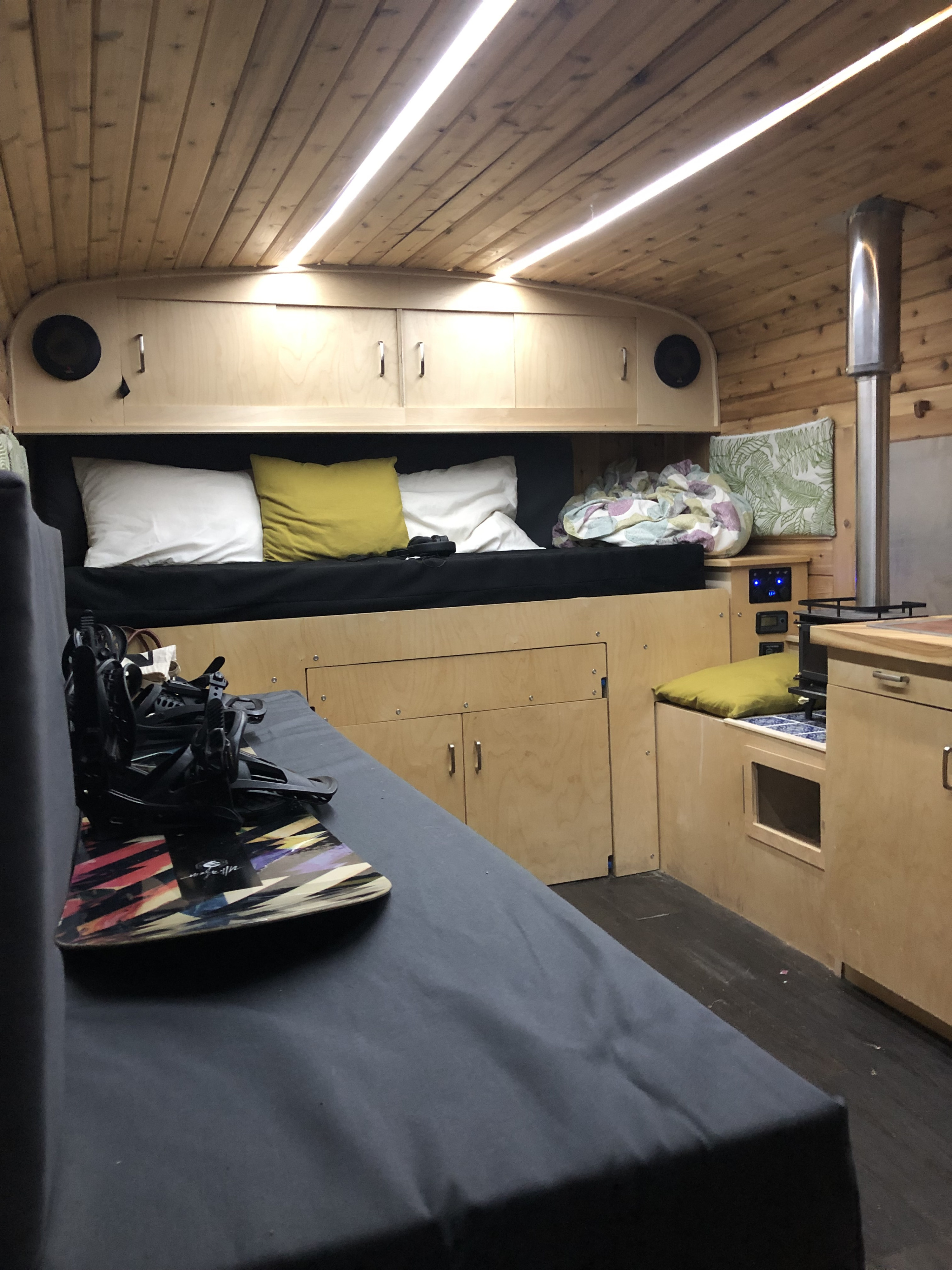 Inside an RV rental: a wood-paneled living space with a bed, kitchen area with a stove, and a snowboard.. Chevrolet Chevrolet Express 1997