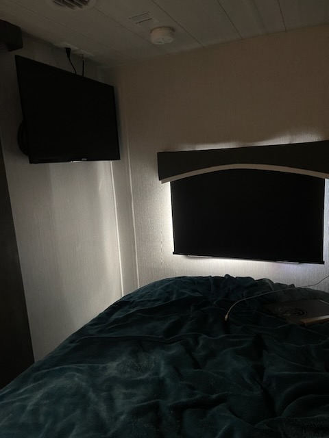 Comfortable RV rental bedroom with two wall-mounted TVs, a soft blanket, and subtle lighting creating a cozy ambiance.. Forest River Evo 2022