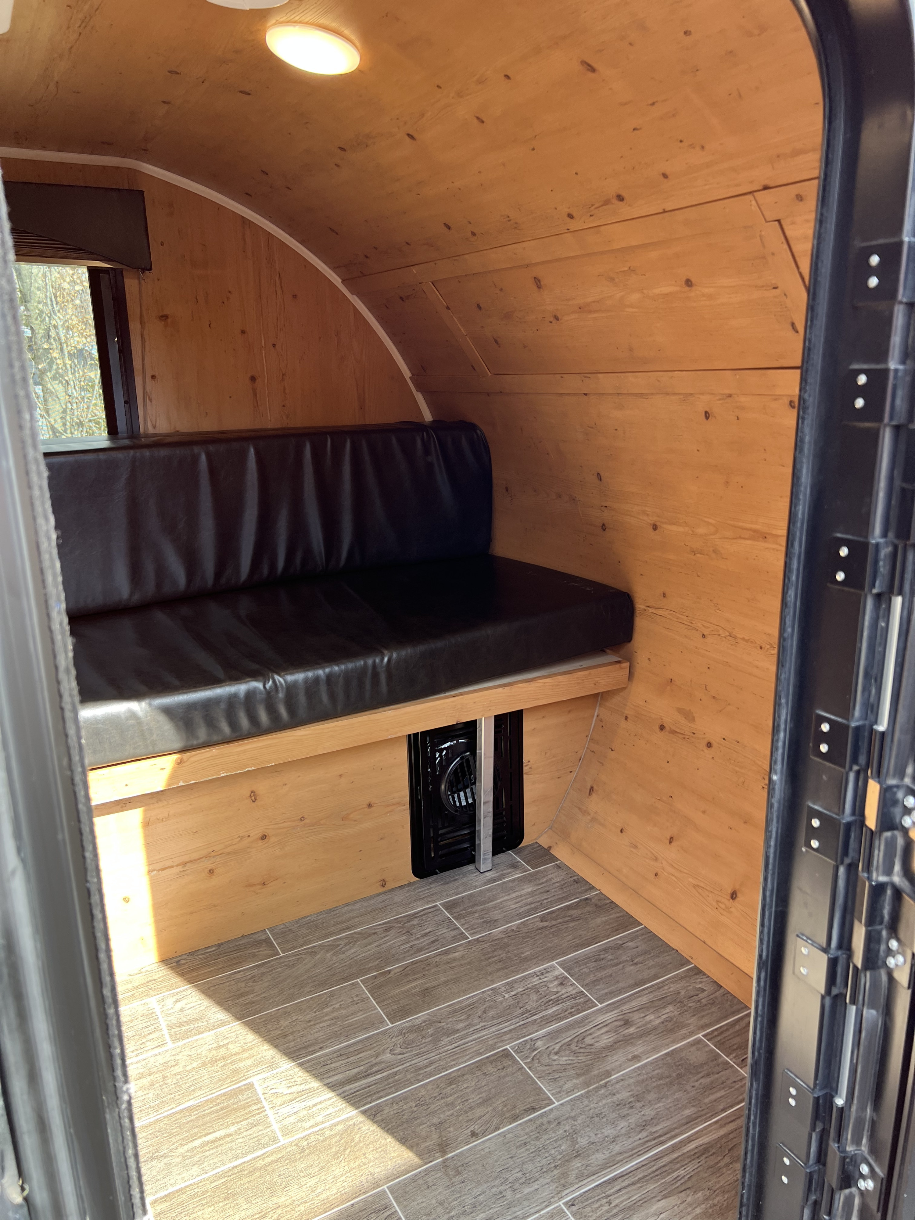 Inside an RV rental: Wooden walls & ceiling, black bench seat, and wood-look tile floor create a cozy camper space.. Sunset Park RV SunRay 2021