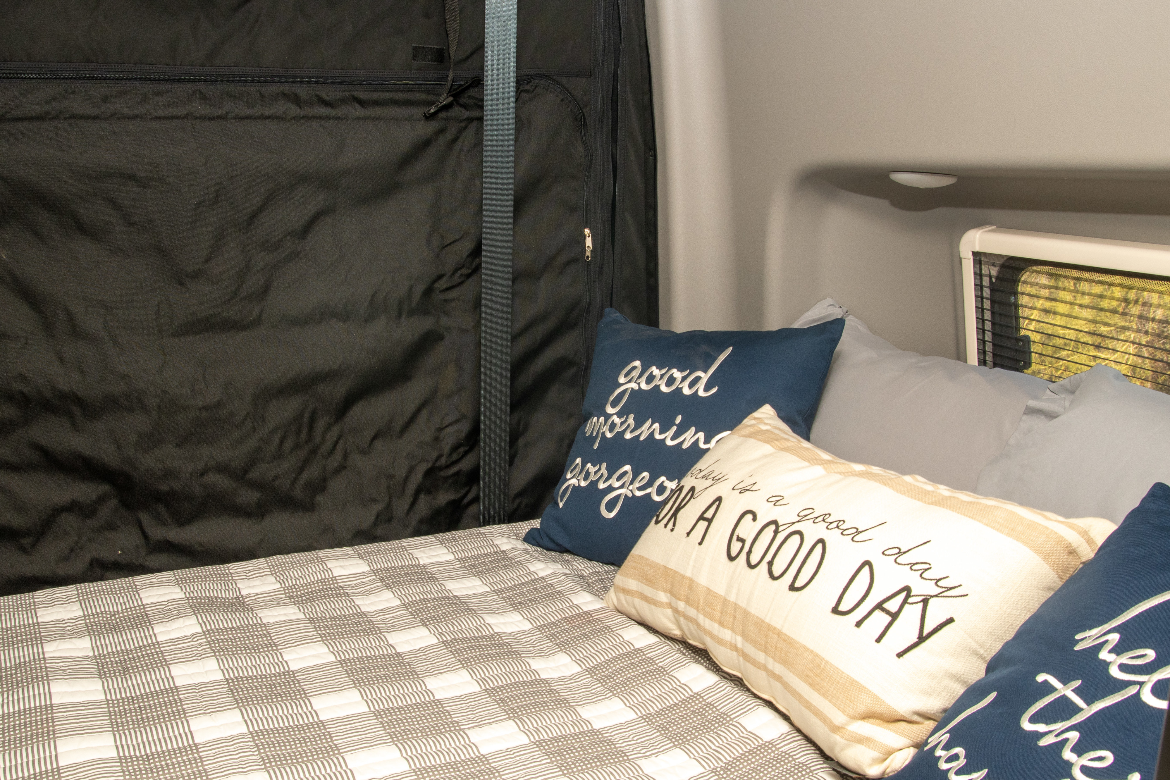 Inside an RV rental: Comfortable bed with plaid quilt, inspiring pillows, and a window view for cozy adventures.. Winnebago Revel 2023