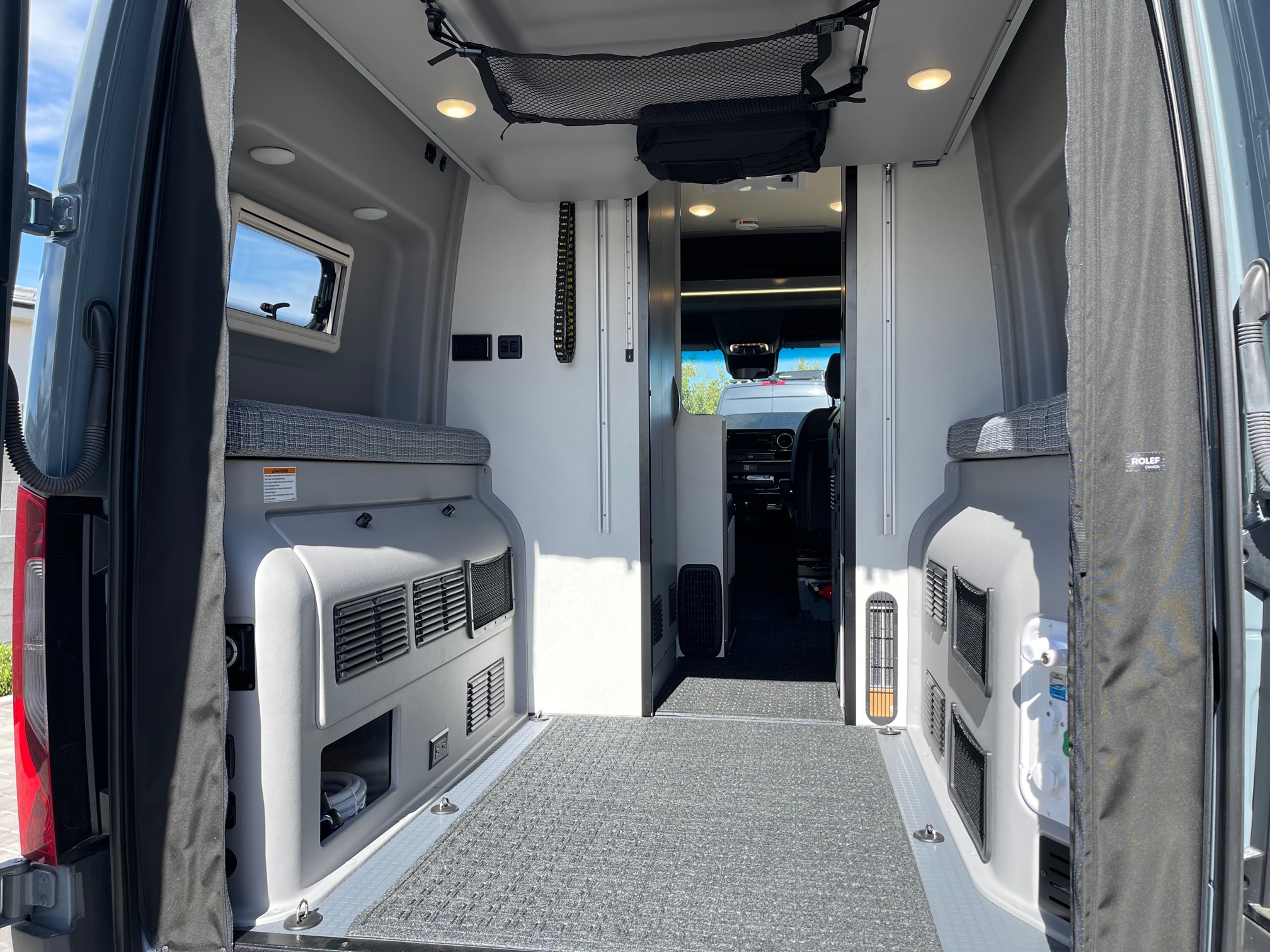 Spacious RV rental interior from the back, showcasing a versatile cargo area, cushioned seating, and built-in storage.. Winnebago Revel 2023