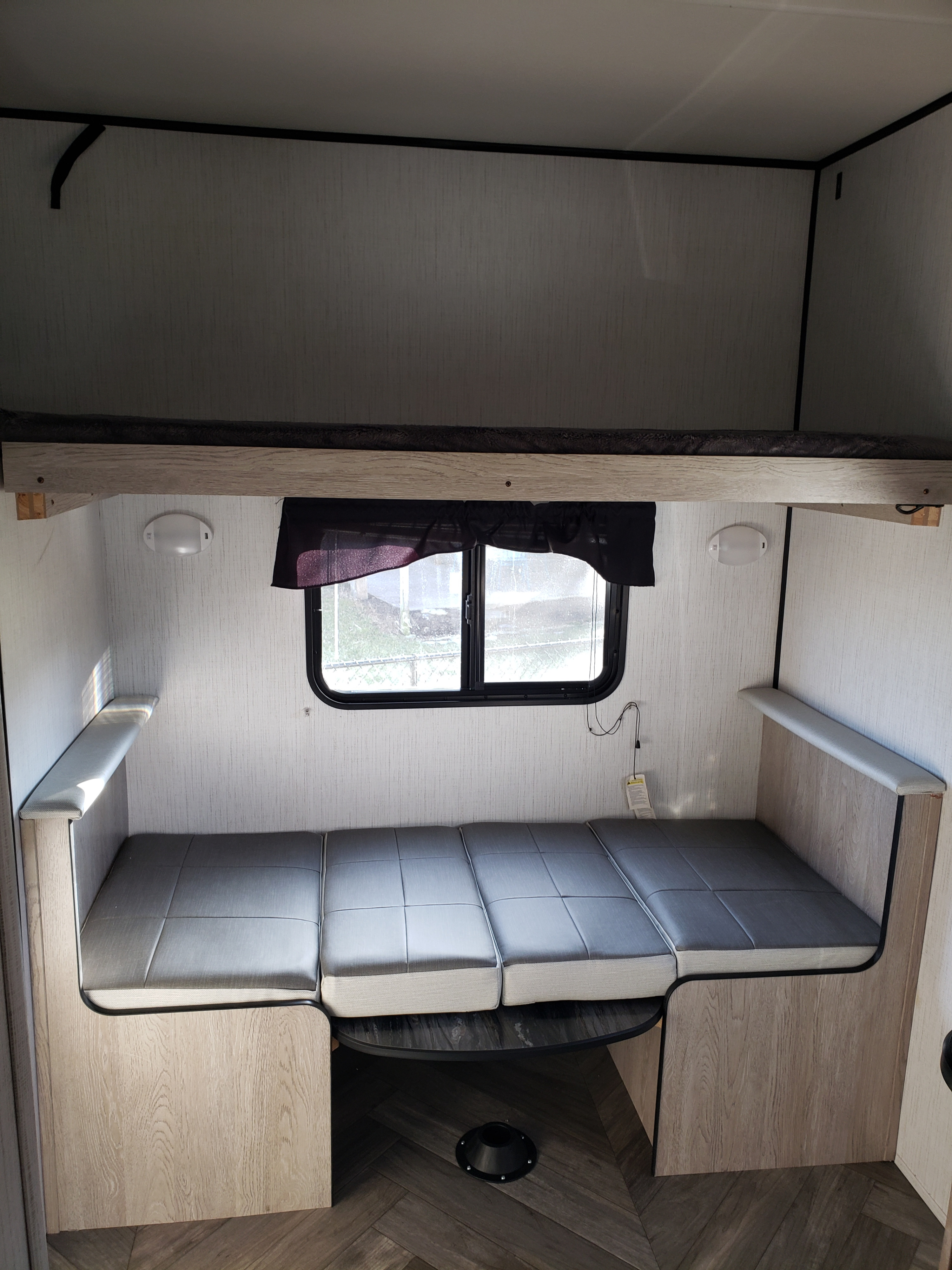 RV rental interior: Top bunk bed, lower convertible dinette with grey cushions, and a window. Compact camper living space.. Heartland RVs Prowler 2022