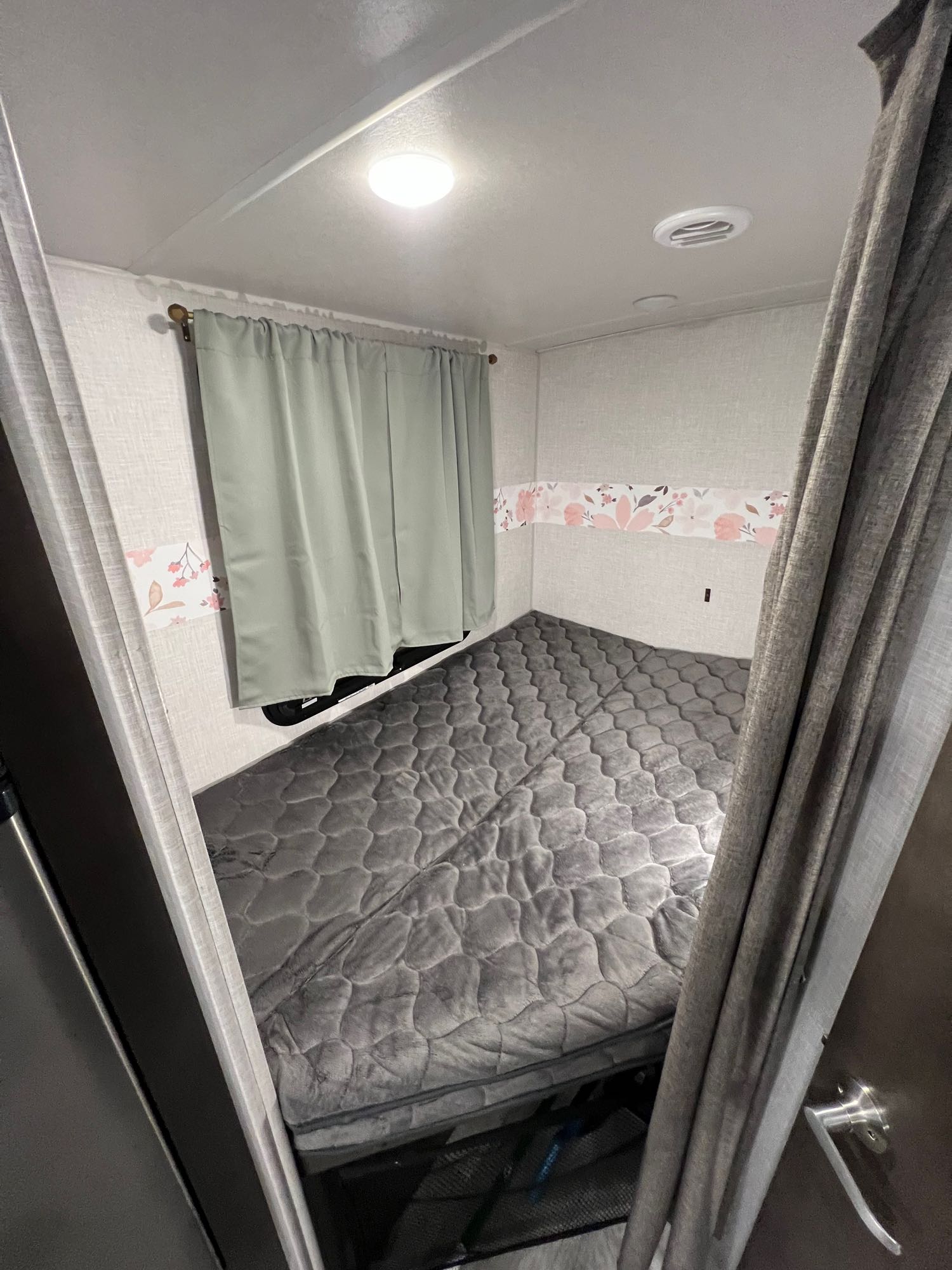 RV rental bedroom: cozy space with grey bed, light, vent, window curtains, and floral wall decor.. Forest River Rockwood Mini Lite 2020