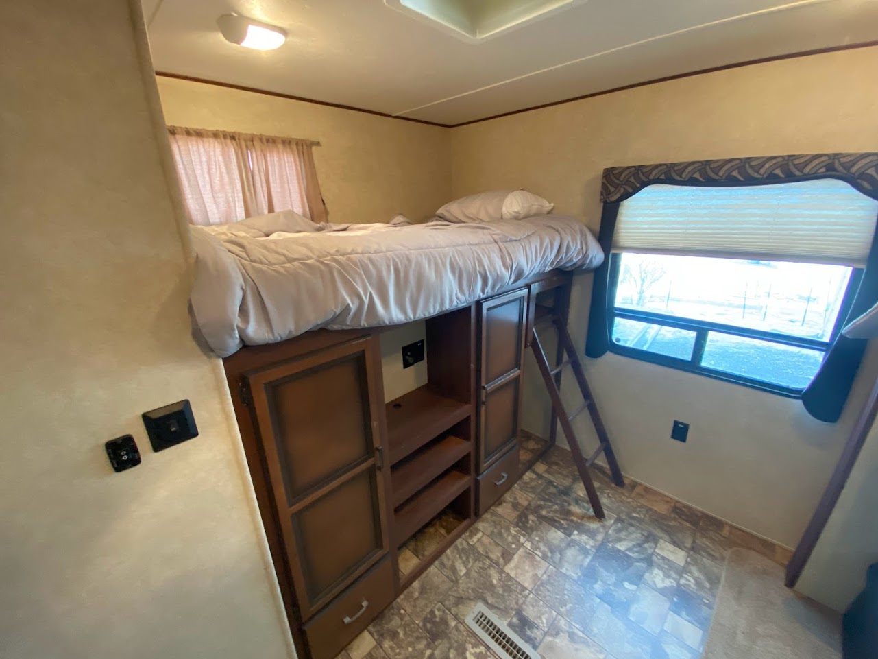 Cozy RV rental bedroom featuring a loft bed over storage, with ladder access and a window.. Crossroads RV Zinger 2013