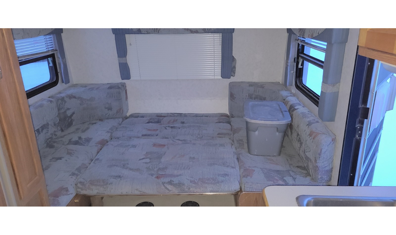 RV rental interior featuring a dinette converted into a bed with patterned cushions, windows, and storage.. Kit 23 Kit Companion 1998