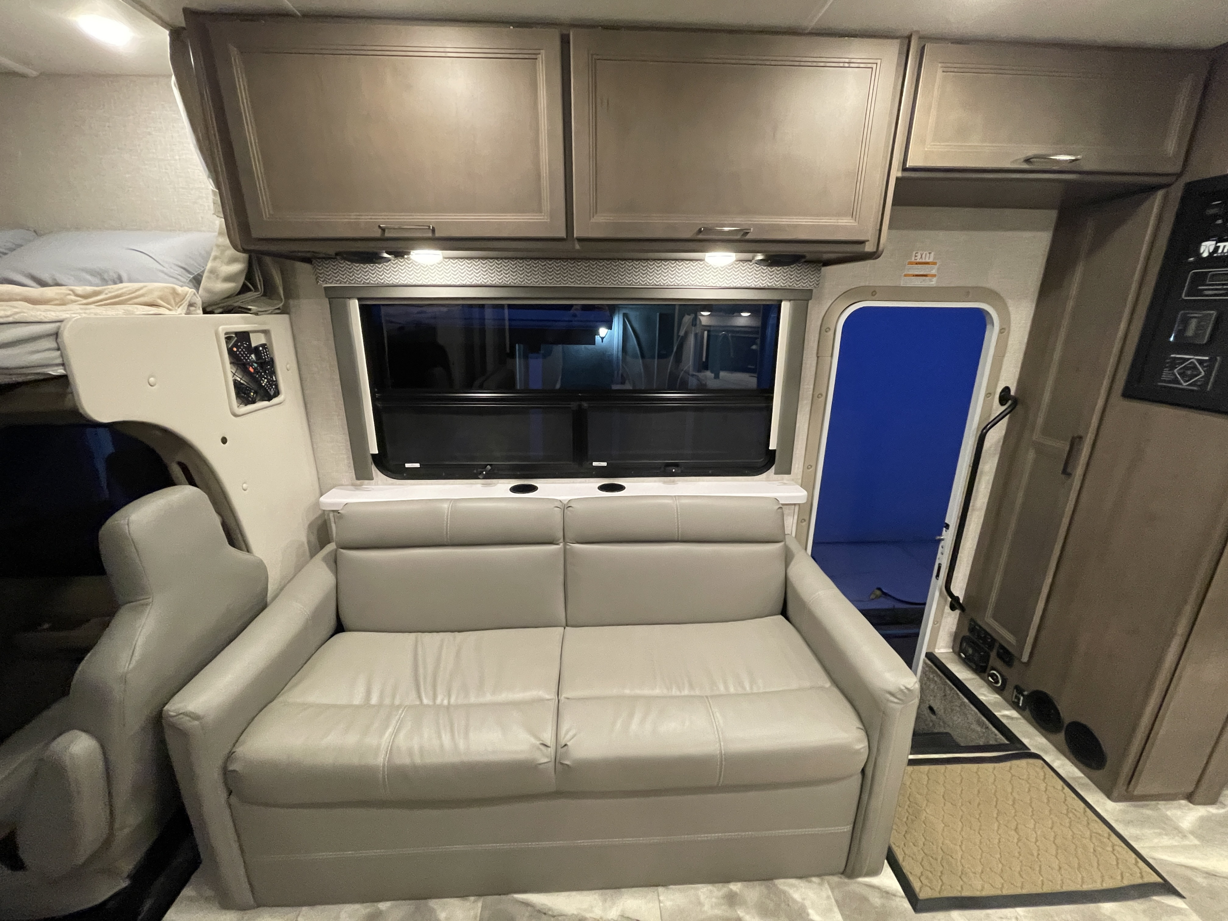 RV rental interior: light grey sofa, overhead bunk bed, storage, and large window.. Thor Motor Coach Quantum 2023