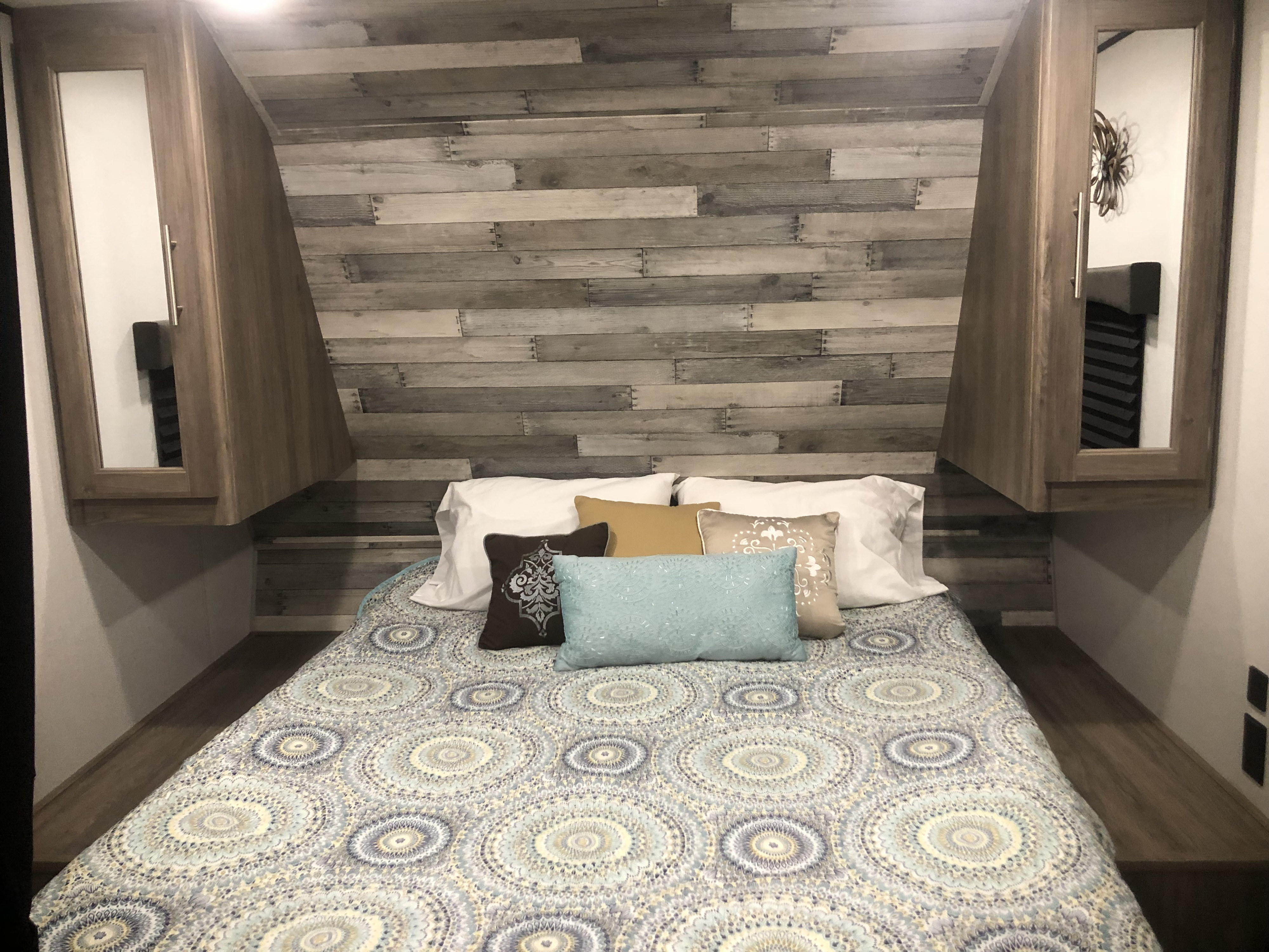 Cozy RV rental bedroom with a patterned queen bed, rustic wood plank wall, and mirrored overhead storage.. Crossroads RV Zinger Lite 2020