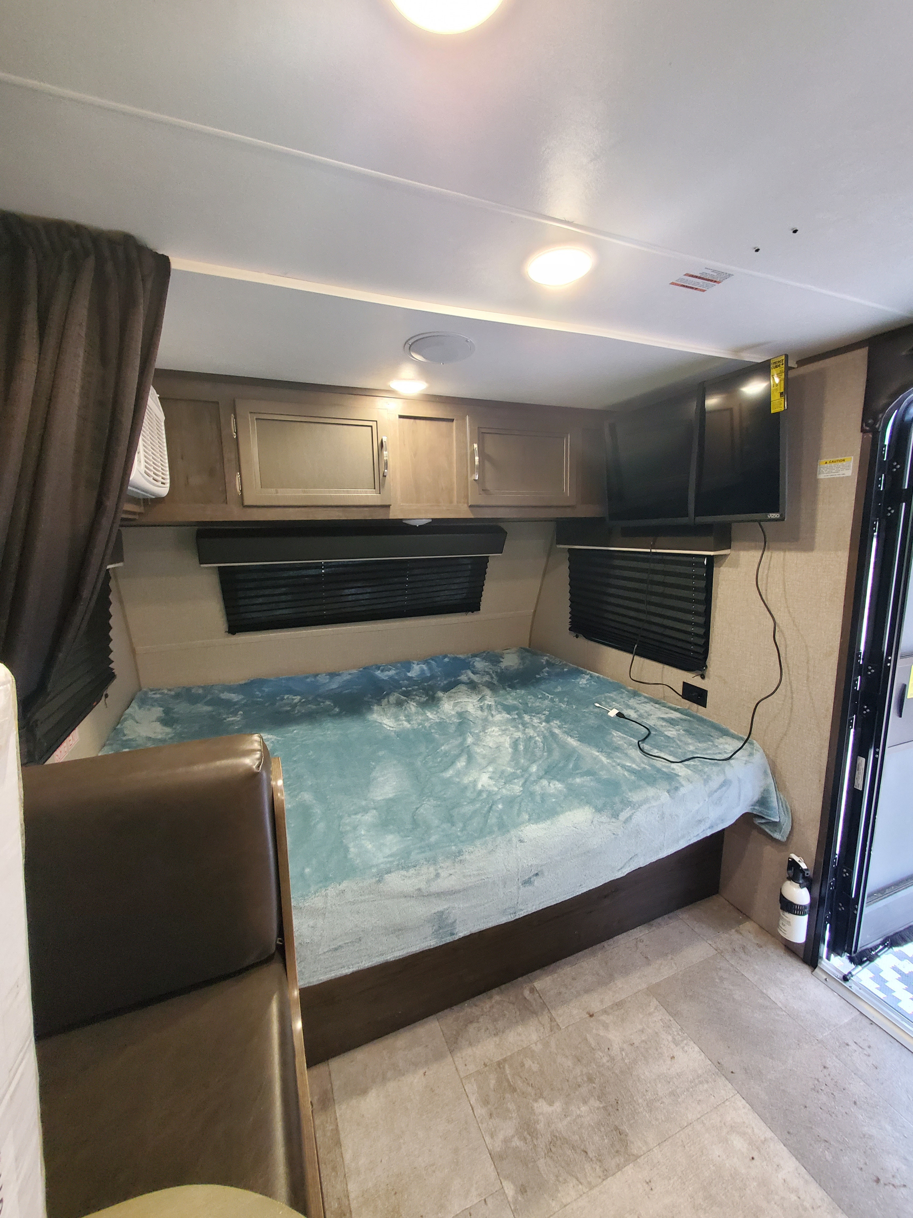 RV rental bedroom with a blue-covered bed, overhead cabinets, TV, and window blinds, designed for compact comfort.. Jayco Jay Flight SLX Baja Edition 2020