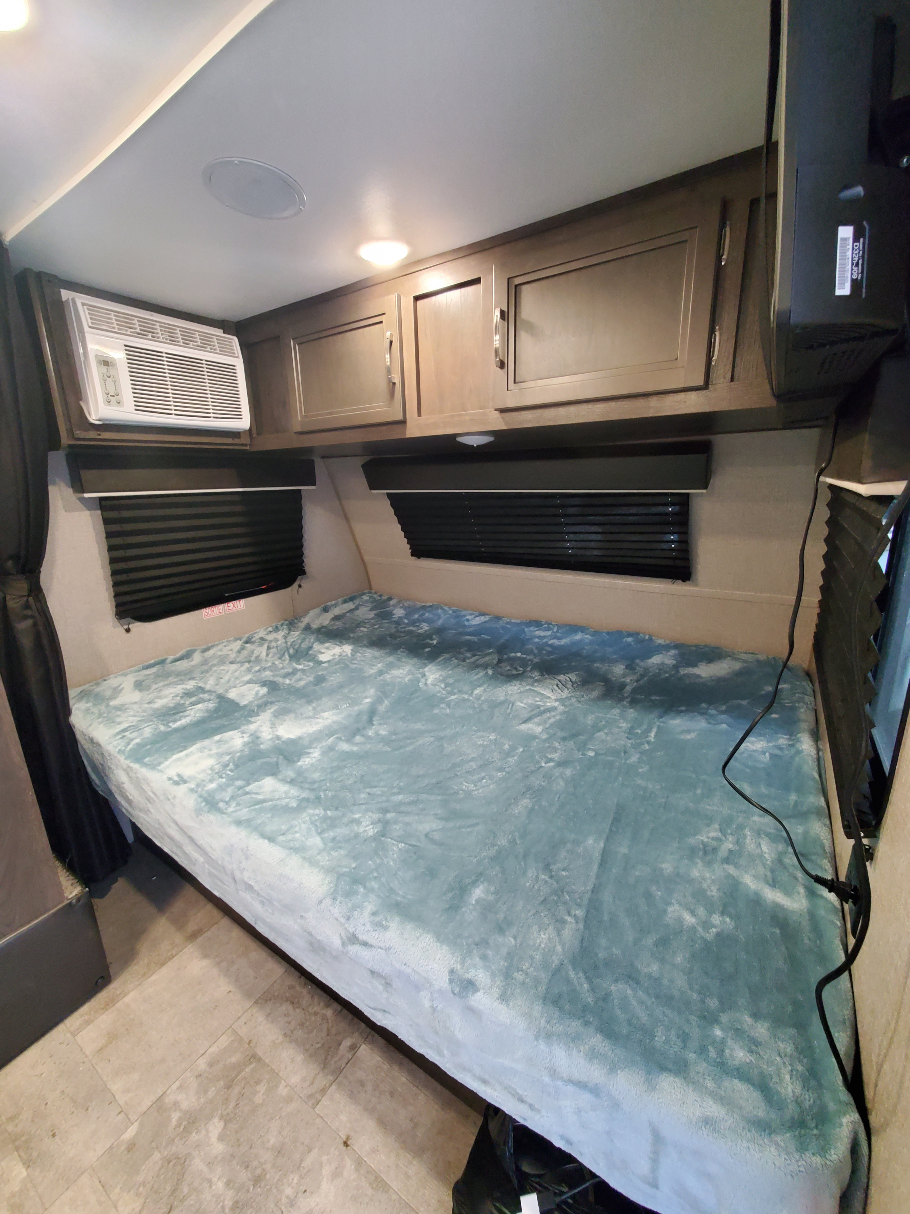 An rv rental bedroom with a large bed, teal blanket, overhead cabinets, AC unit, and wall-mounted TV.. Jayco Jay Flight SLX Baja Edition 2020