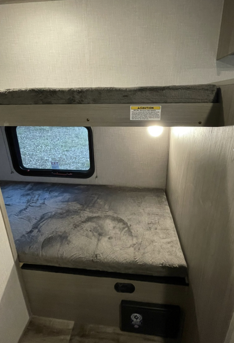 Cozy bunk beds with plush grey mattresses fill this RV rental, offering a window and reading lights for comfortable travel.. Other Other 2021