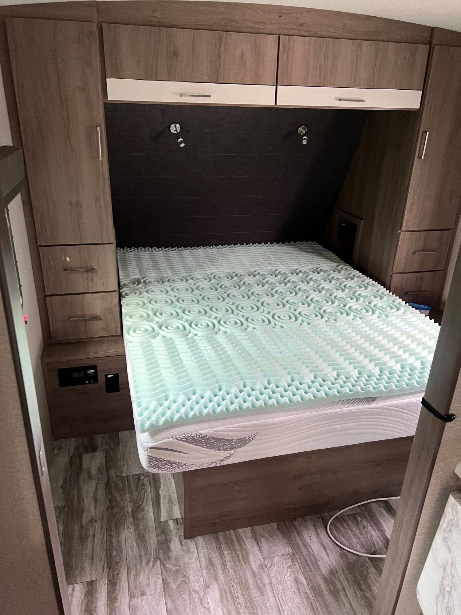 Cozy RV rental bedroom with a bed featuring a light green foam mattress topper, ample storage, and built-in lighting.. Grand Design Imagine 2022