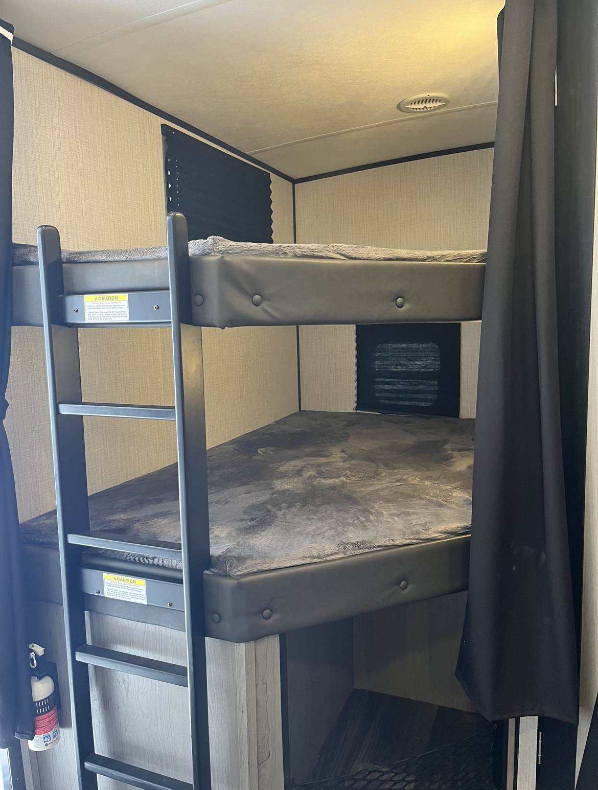 Inside an RV rental, showing compact bunk beds with a ladder & soft grey blankets, ideal for family sleeping quarters.. Heartland RVs Mallard 2021