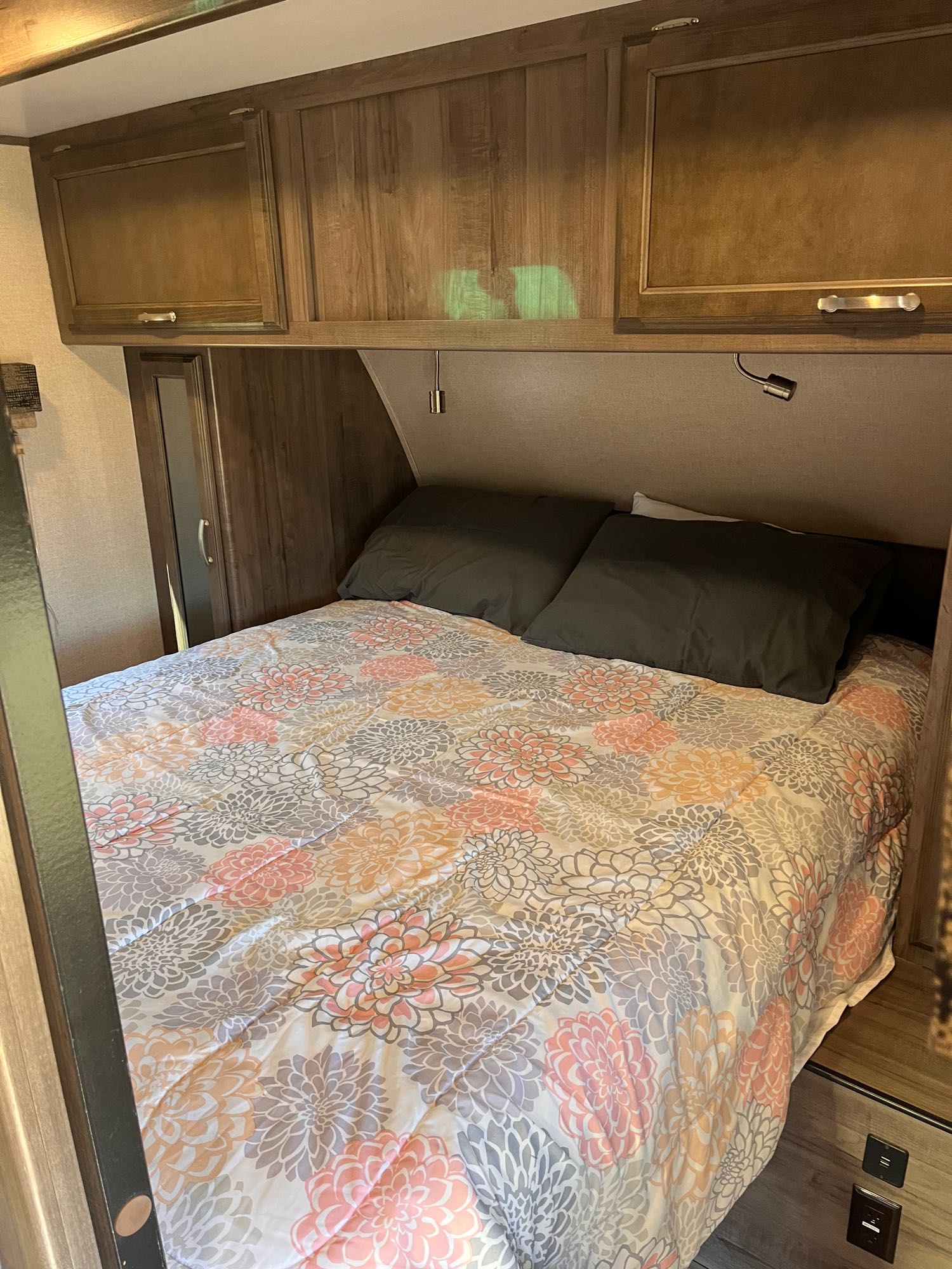 Cozy RV rental bedroom: bed with floral comforter, dark pillows, wood cabinetry, and reading lights for comfortable travel.. Minnie Minnie Plus 2019