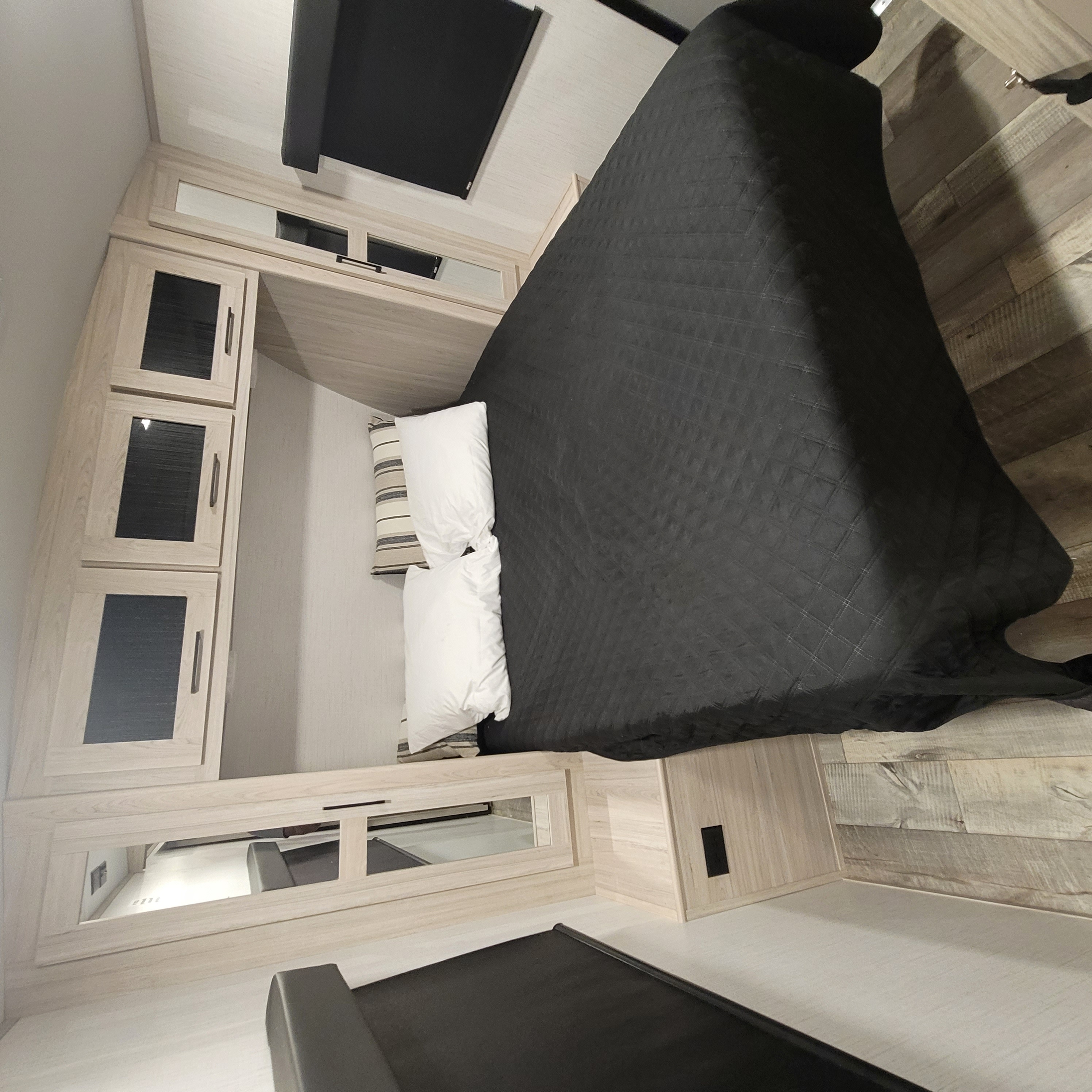 Comfortable RV rental bedroom with a dark comforter, white and striped pillows, and light wood cabinetry with dark glass inserts.. Heartland RVs Sundance Ultra Lite 2022