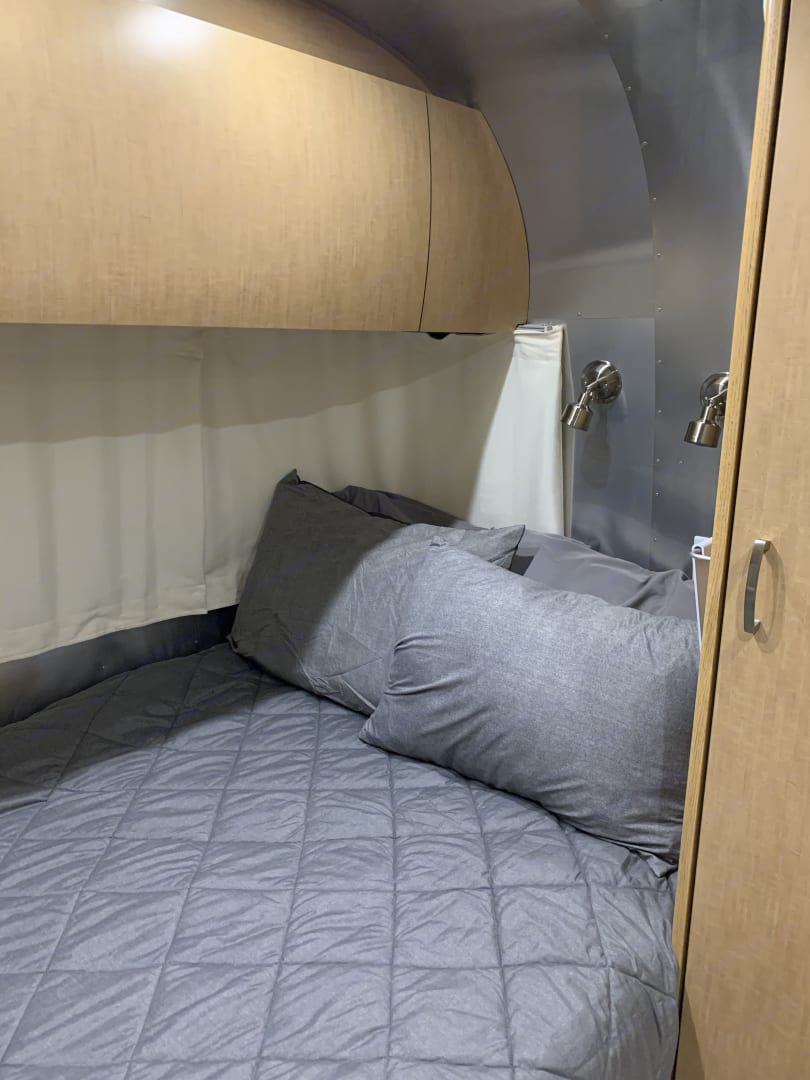 Cozy RV rental bedroom with gray quilted bed, wooden cabinets, and metal walls with reading lights.. Airstream Flying Cloud 2012
