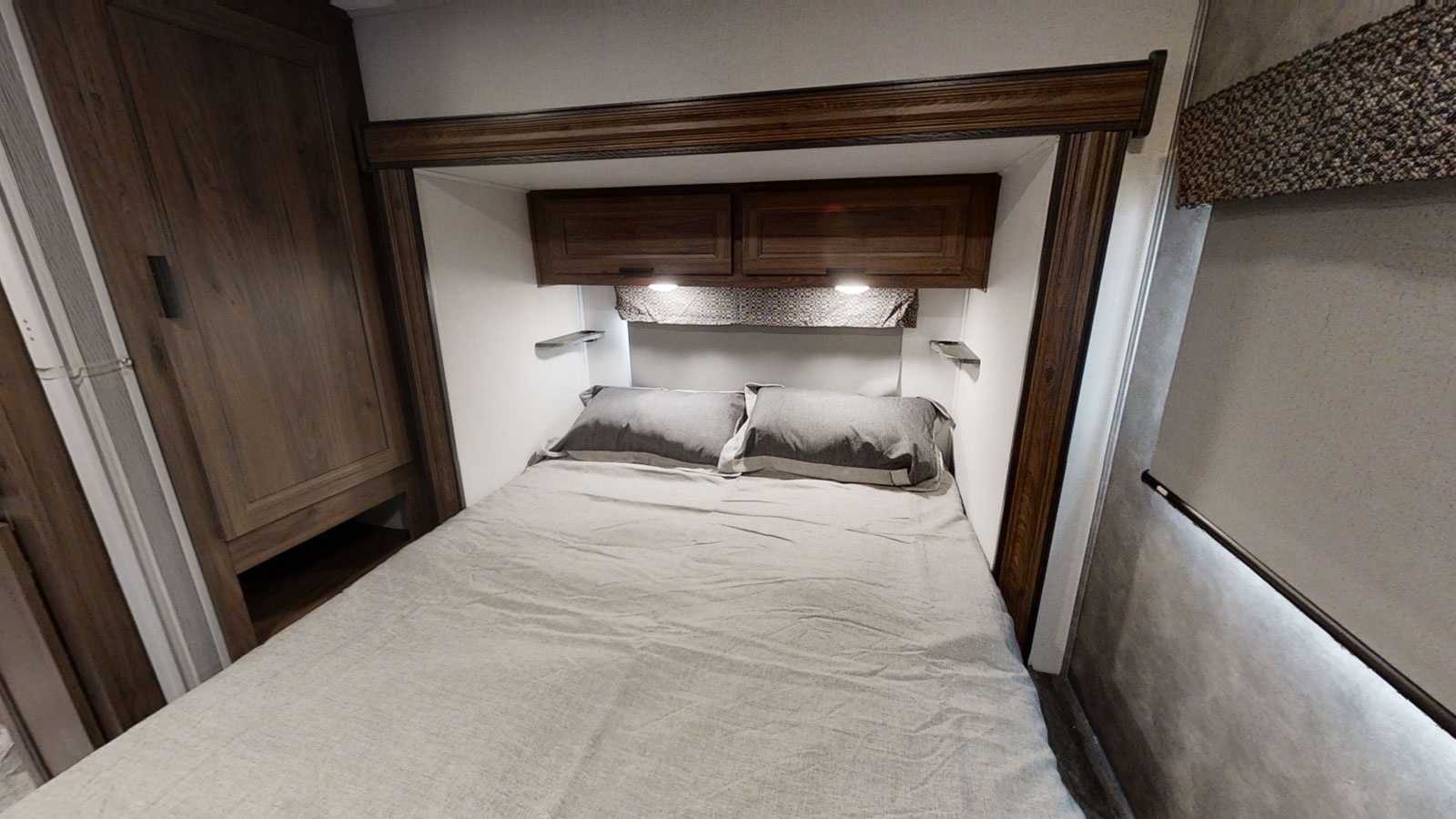 A welcoming RV rental bedroom features a queen bed with grey bedding, dark wood cabinets, and built-in wardrobe.. Forest River Sunseeker 2024