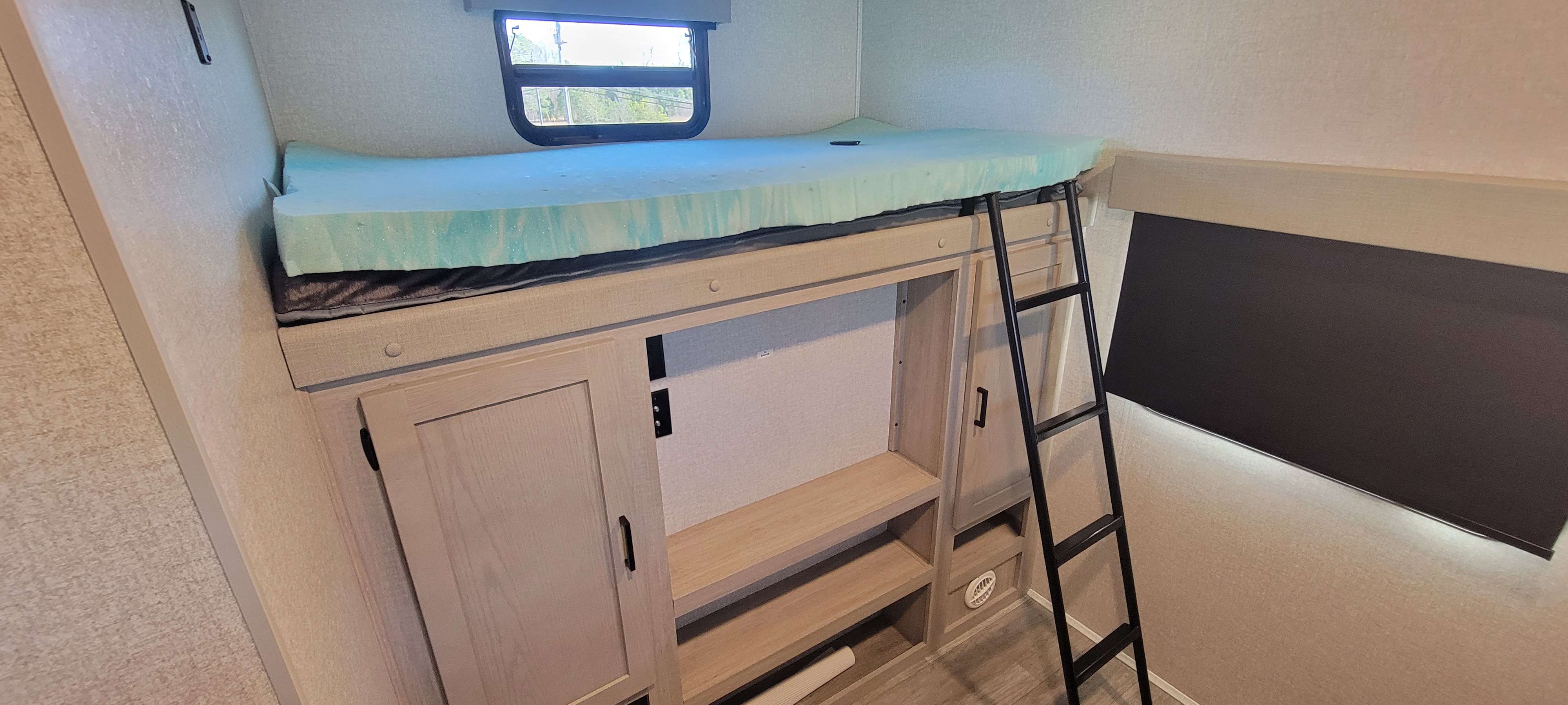 RV rental bunk bed area: light blue foam mattress, access ladder, window, and integrated storage cabinets below.. East to West Alta 2022