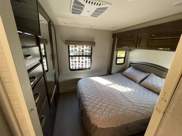 Cozy rv rental bedroom features a large quilted bed, built-in storage/dresser, and sunlit window. Perfect for travelers.. Jayco Greyhawk 2018