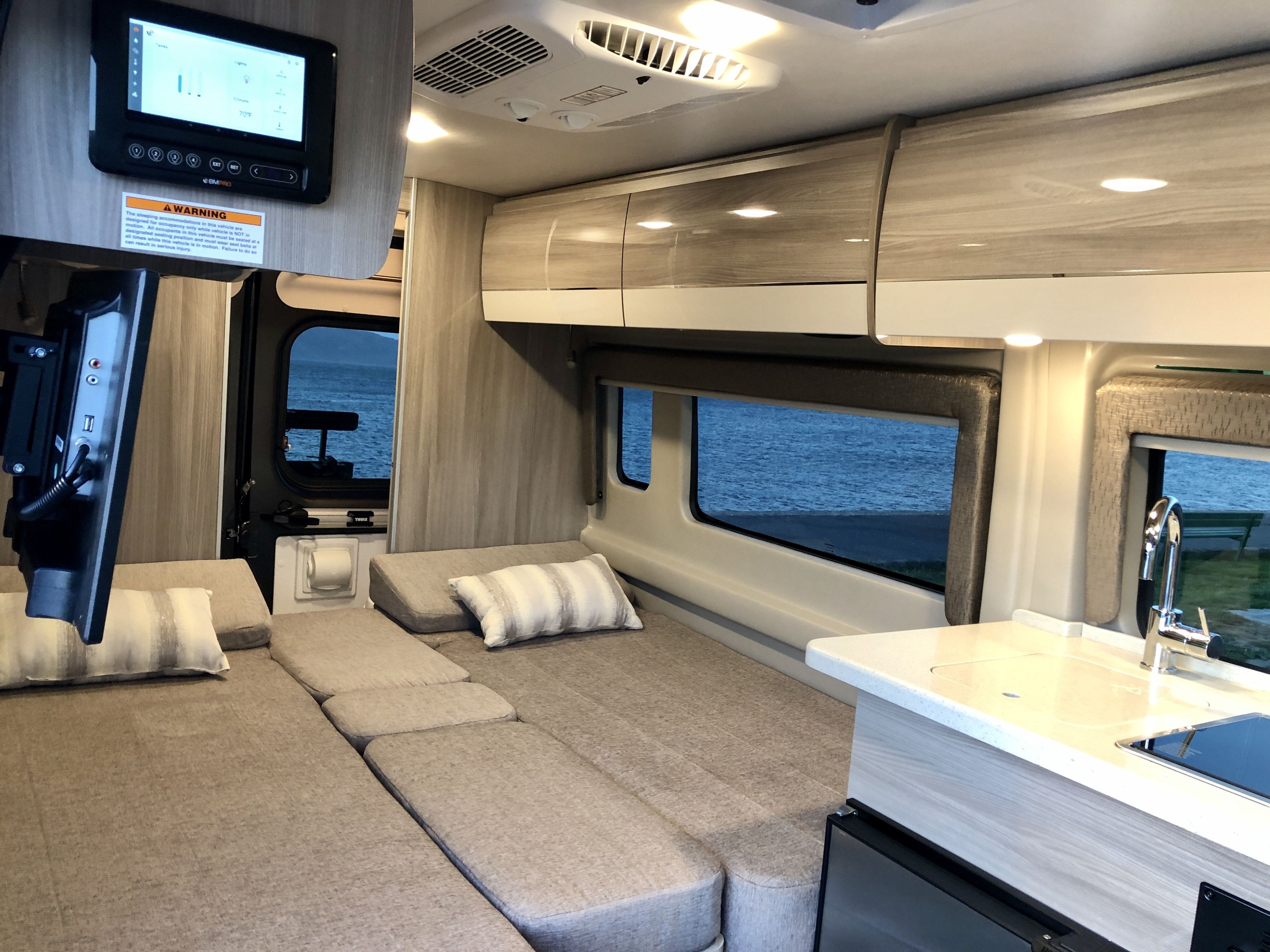Spacious RV rental interior with multi-purpose seating/bed, compact kitchen, and digital control panel overlooking water.. Thor Sequence 2021