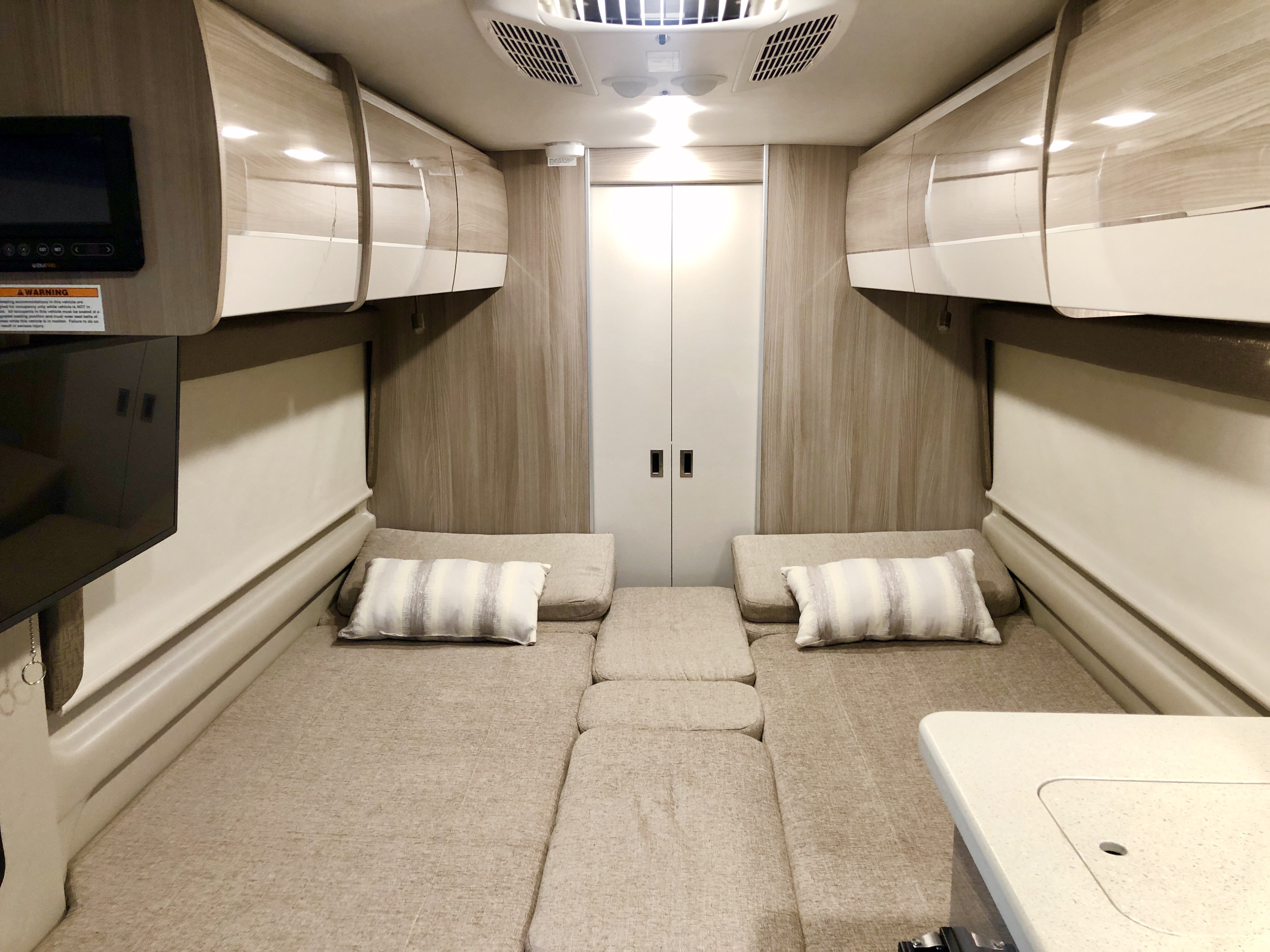 Spacious RV rental interior featuring convertible beds, ample overhead storage, TV, and a functional tabletop, ideal for comfortable road trips.. Thor Sequence 2021