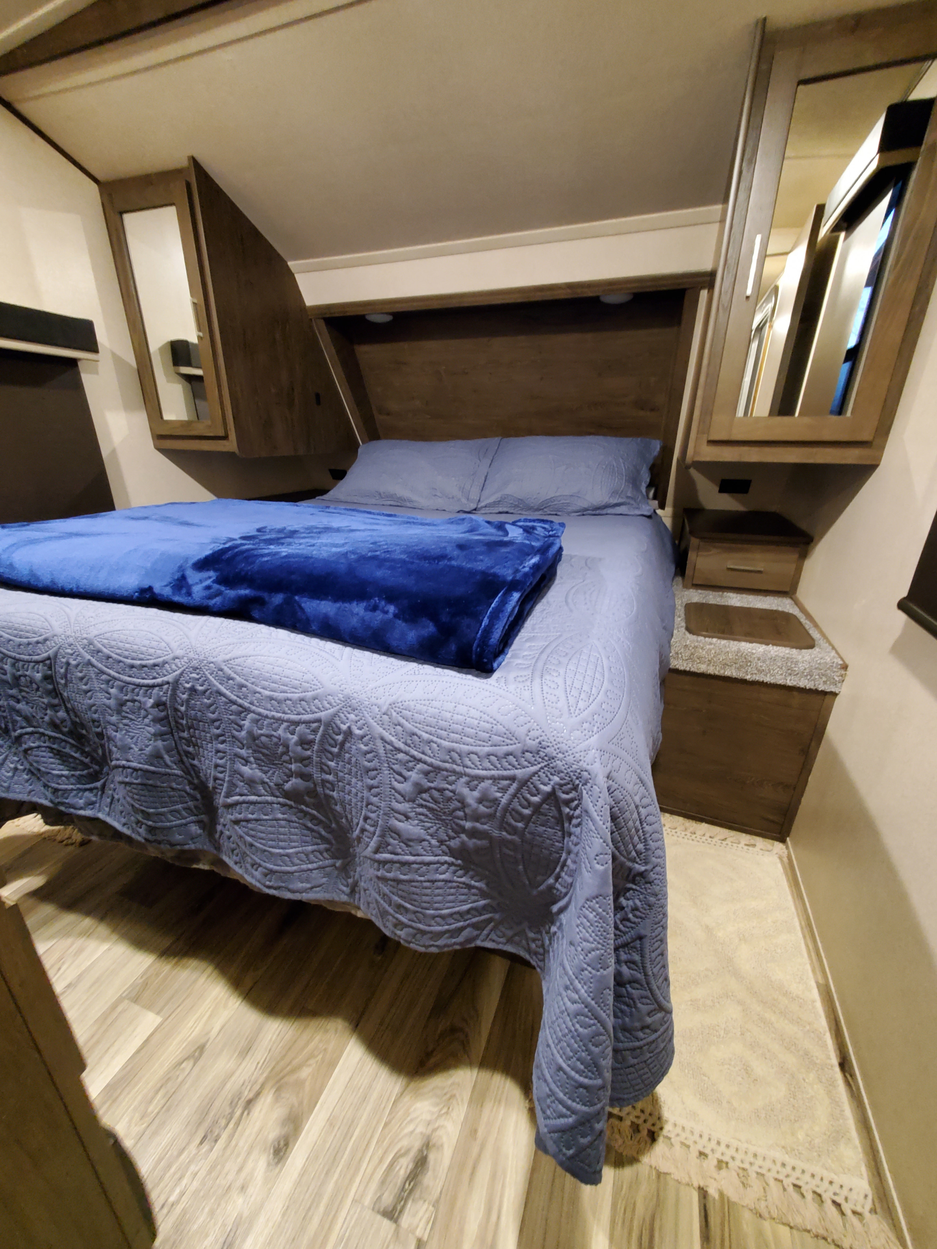 This cozy RV rental bedroom features a bed with blue bedding, mirrored cabinets, and efficient storage.. Forest River Wildwood 2019