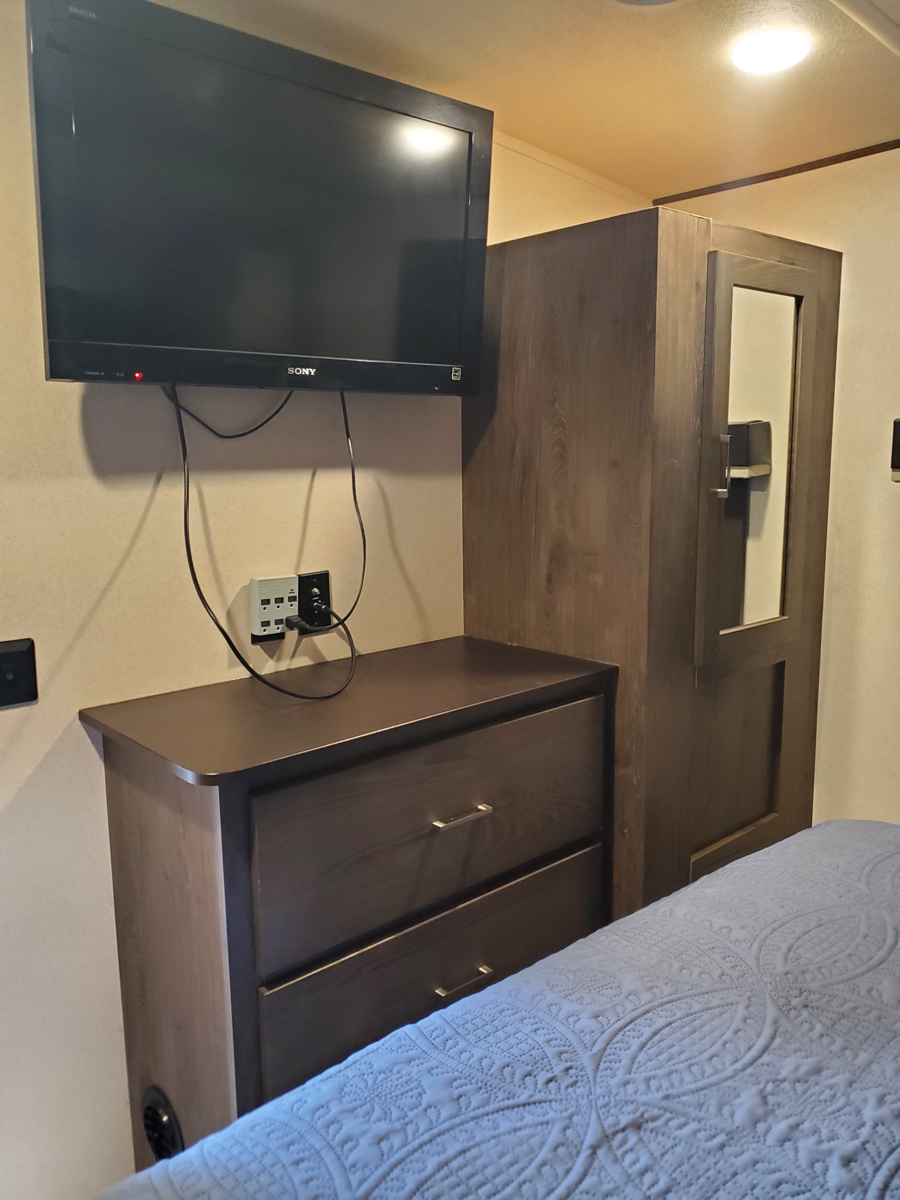 RV rental bedroom featuring a mounted Sony TV, dresser, and mirrored wardrobe, providing storage & entertainment.. Forest River Wildwood 2019