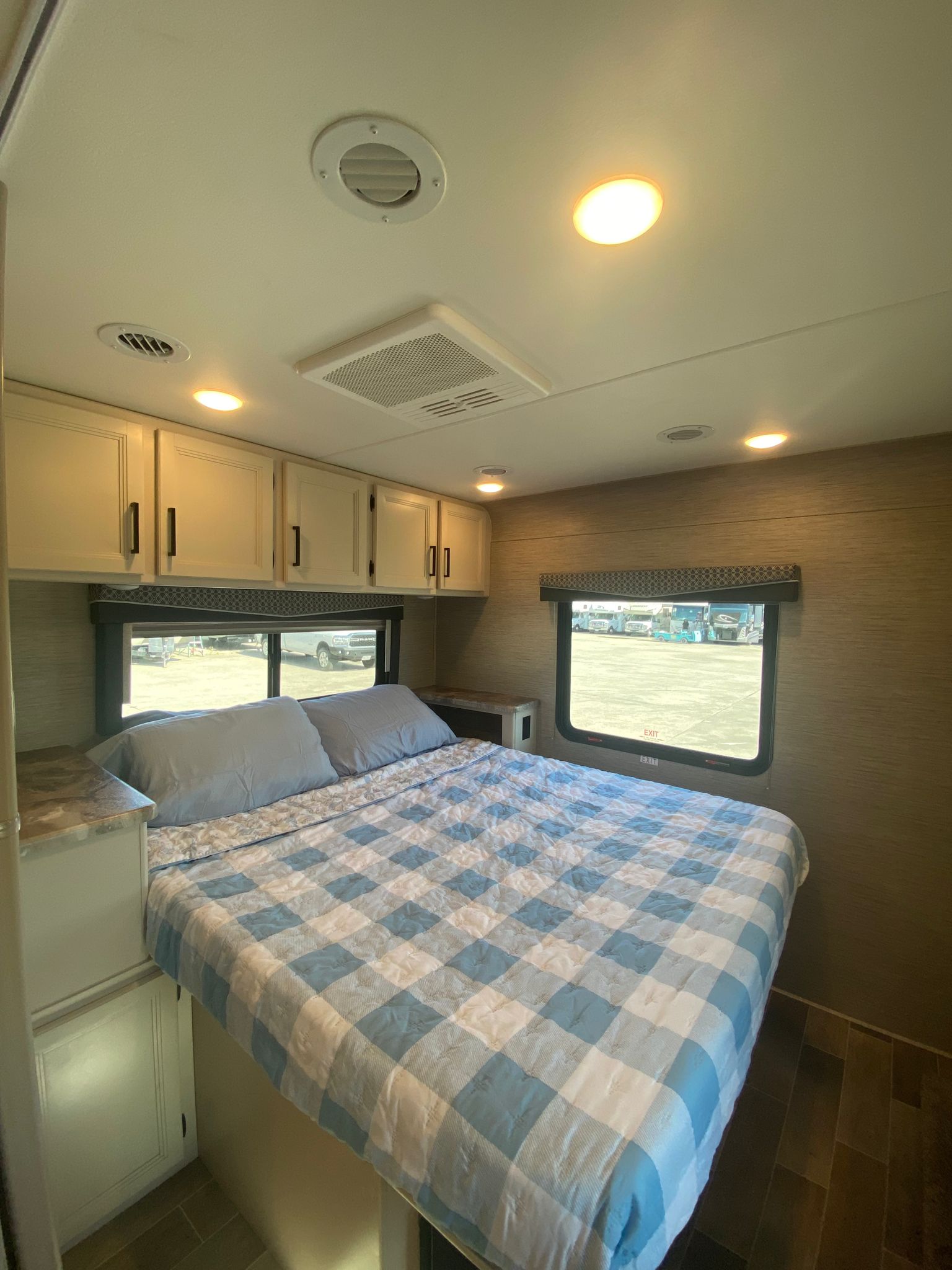 Cozy RV rental bedroom featuring a checked bed, overhead cabinets, and bright windows with an outdoor view.. Thor Motor Coach Chateau 2022